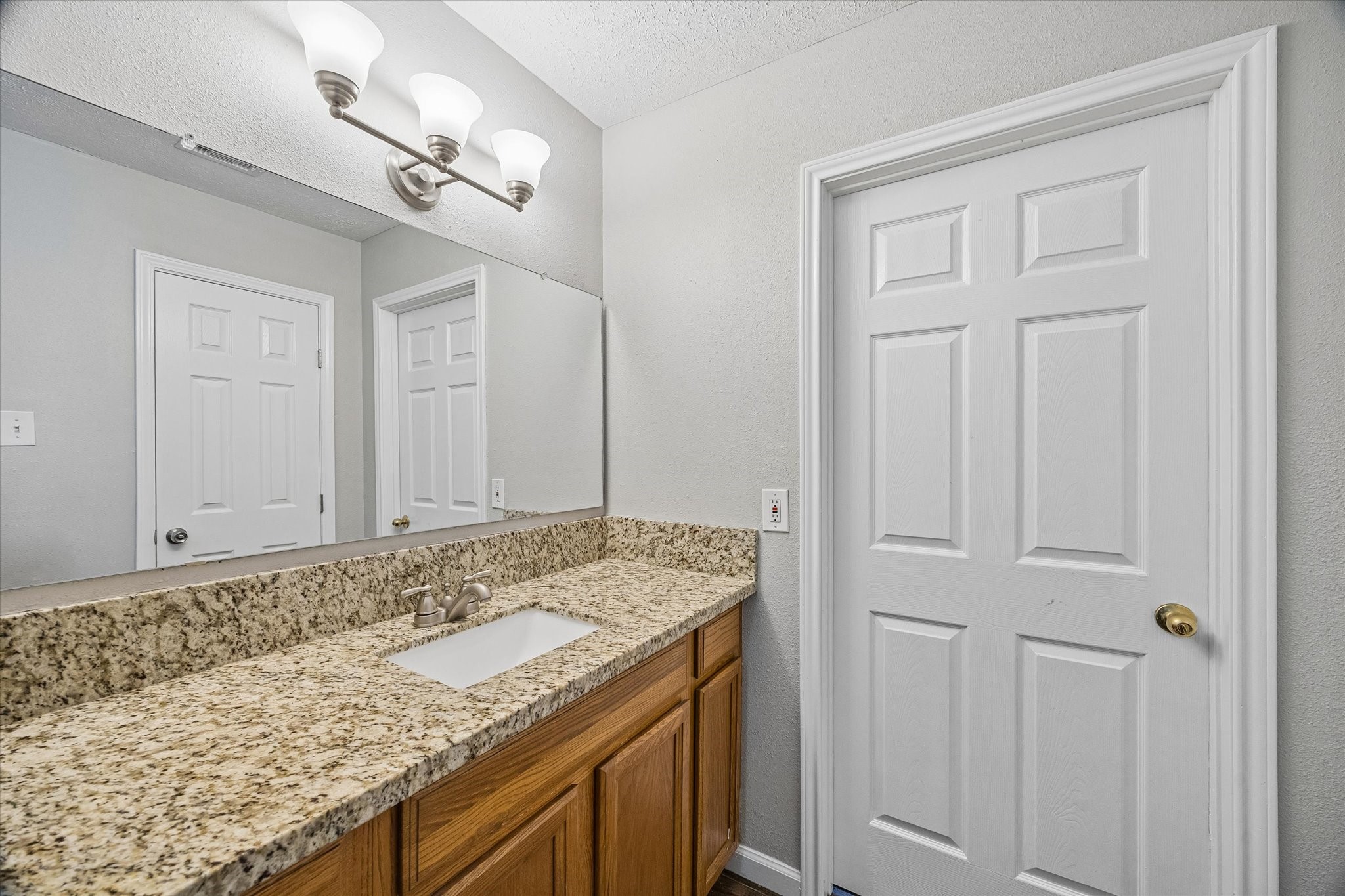 Elegant bathroom featuring a granite countertop, large mirror, and modern lighting, providing both style and functionality.