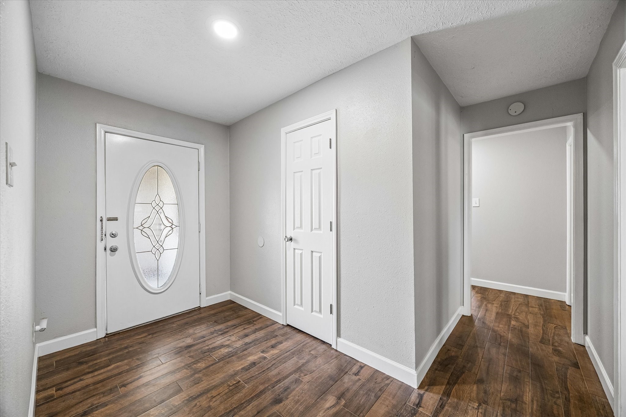 Inviting entryway with elegant wood like tile flooring, a stylish oval glass front door, and neutral walls, leading to a spacious interior.