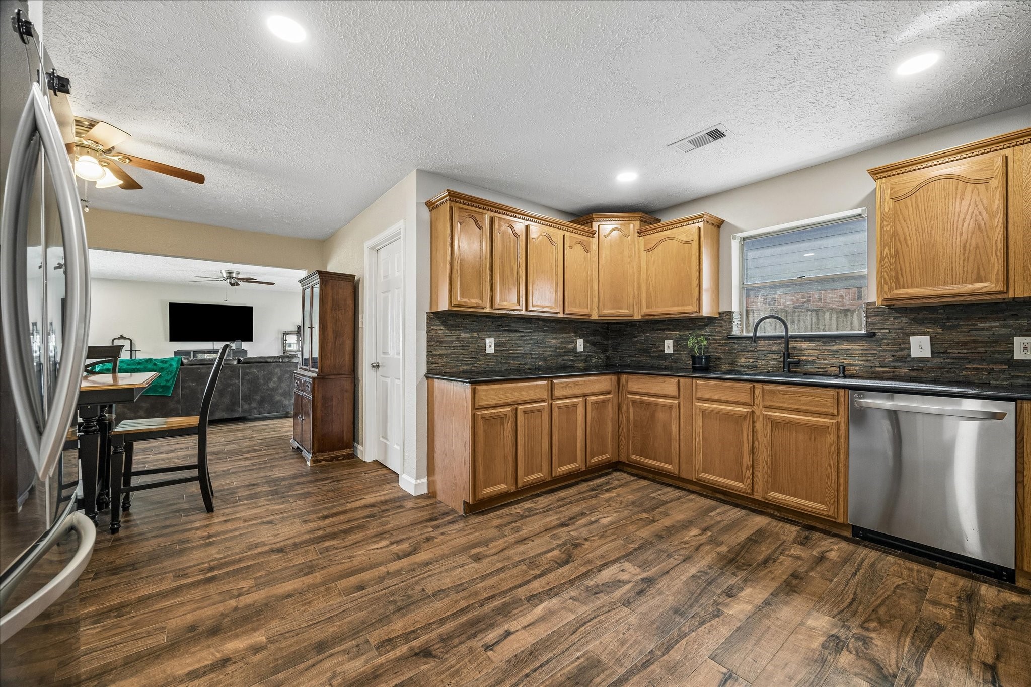 The spacious kitchen features rich wood cabinetry, sleek stainless steel appliances, and a stylish stone backsplash, creating a warm and inviting space that blends functionality with timeless appeal.