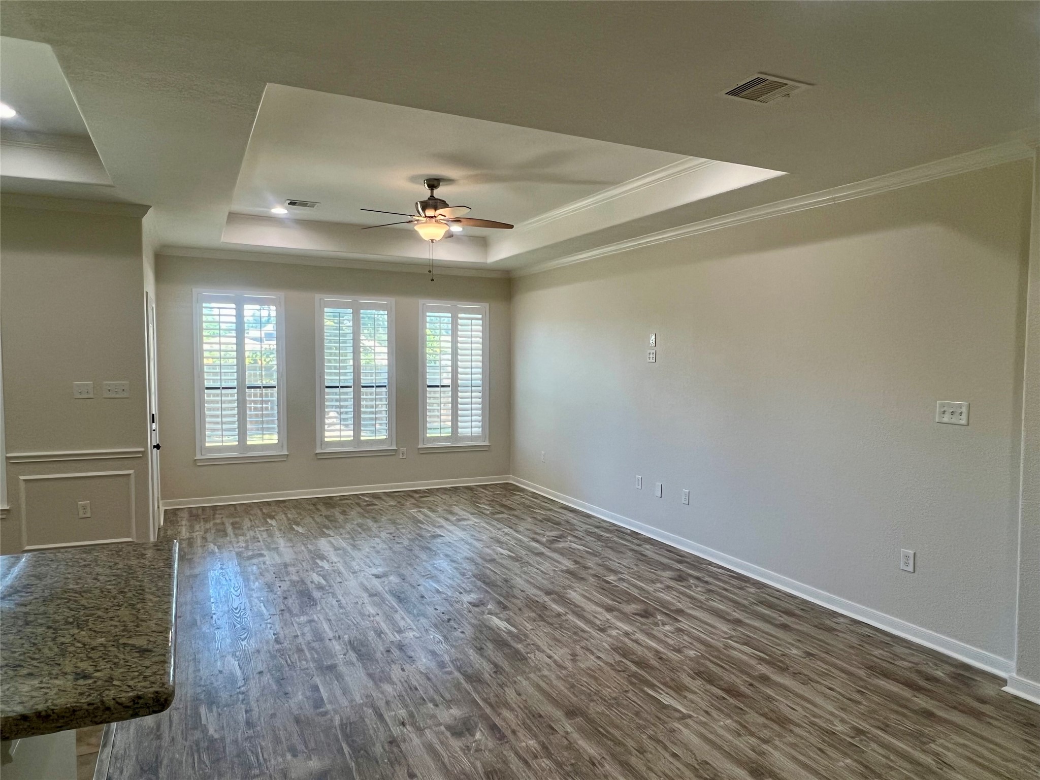 Another view of living area with tray ceiling, plantation shutters, and easy to clean vinyl plank flooring. Another view of living area with tray ceiling, plantation shutters, and easy to clean vinyl plank flooring.