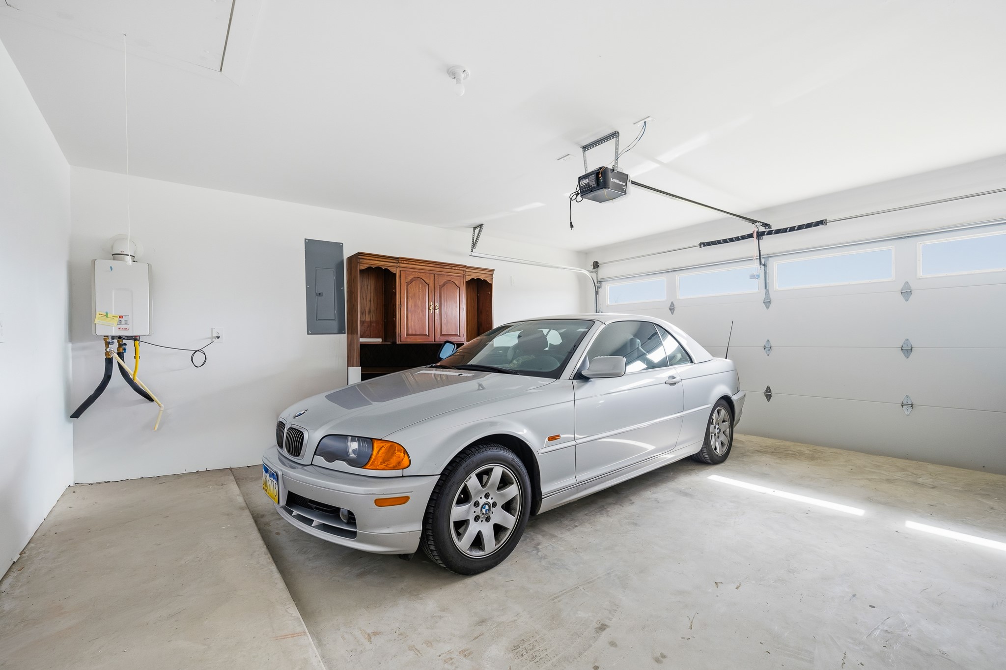 This spacious garage features a clean, bright interior with a water heater and storage cabinet. It includes a large automatic door, accommodating two vehicles comfortably.