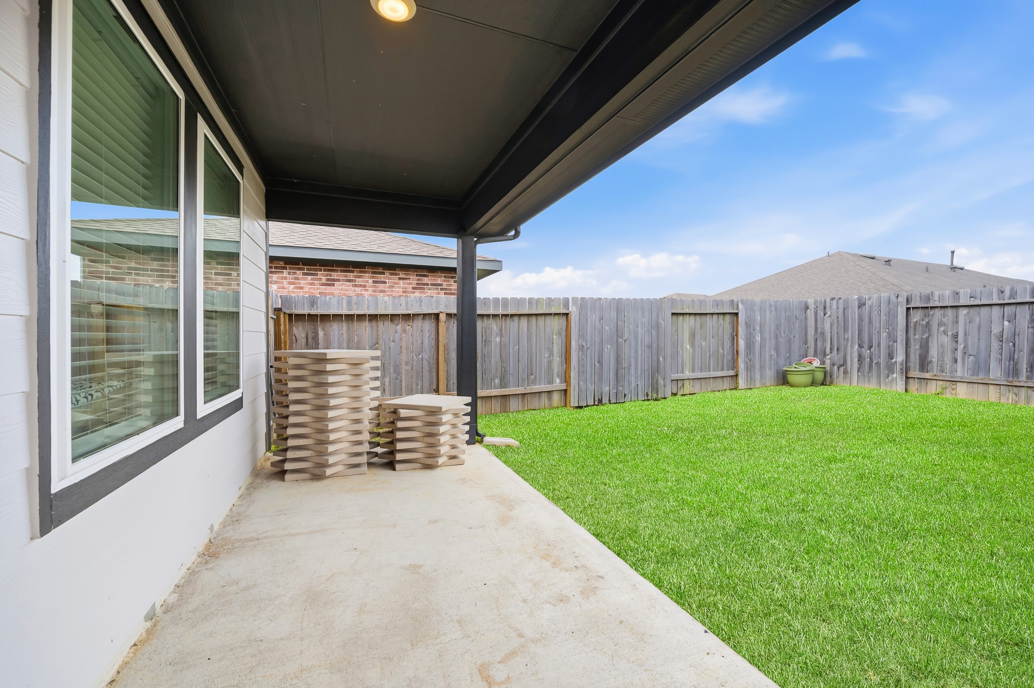This photo showcases a covered patio with a concrete floor overlooking a well-maintained, fenced backyard with green grass. It's ideal for outdoor relaxation and entertaining.
