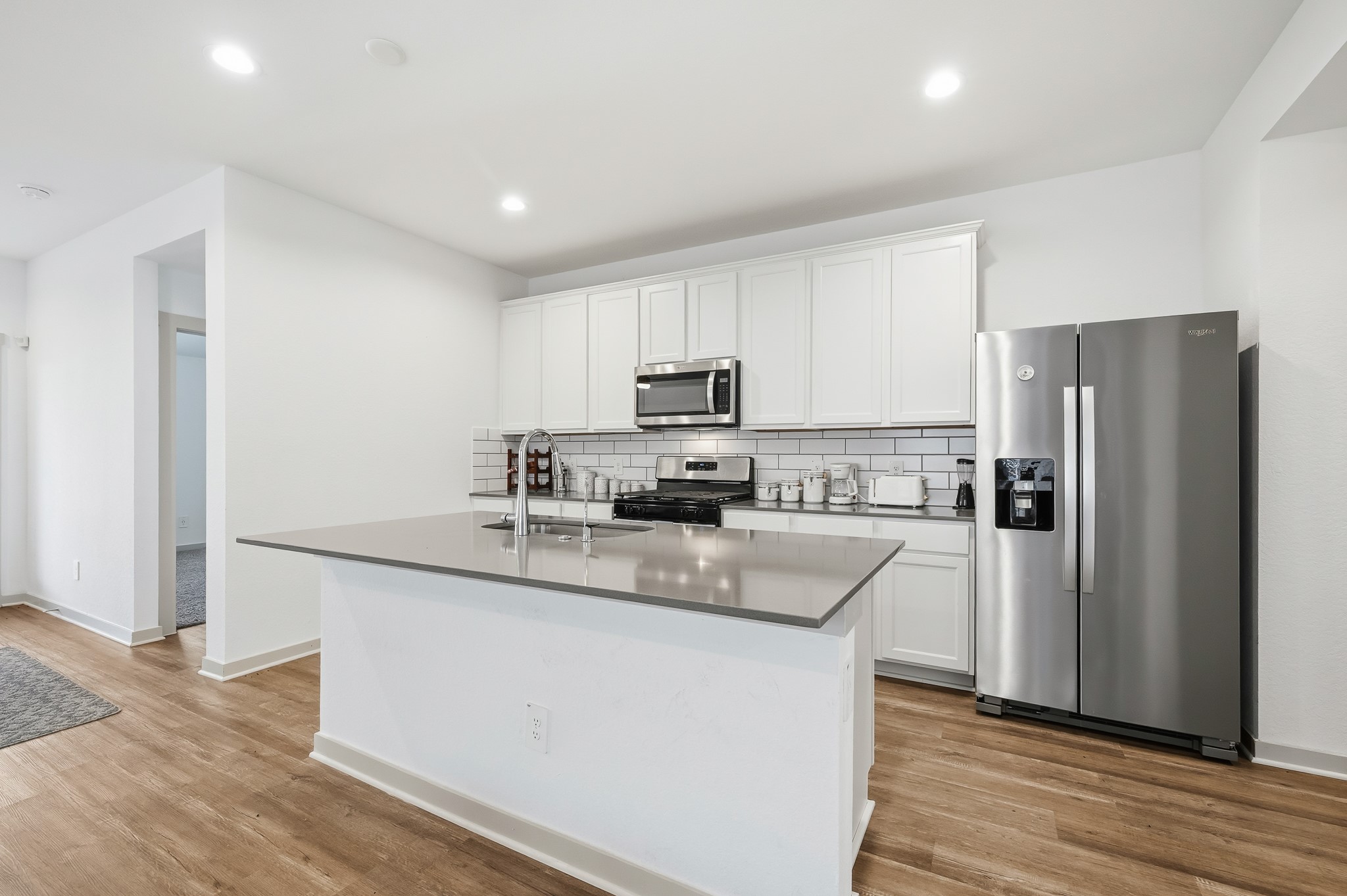 Modern kitchen with sleek stainless steel appliances, white cabinetry, and a stylish subway tile backsplash. Features a spacious island with a smooth countertop and wood flooring for a warm, inviting atmosphere.