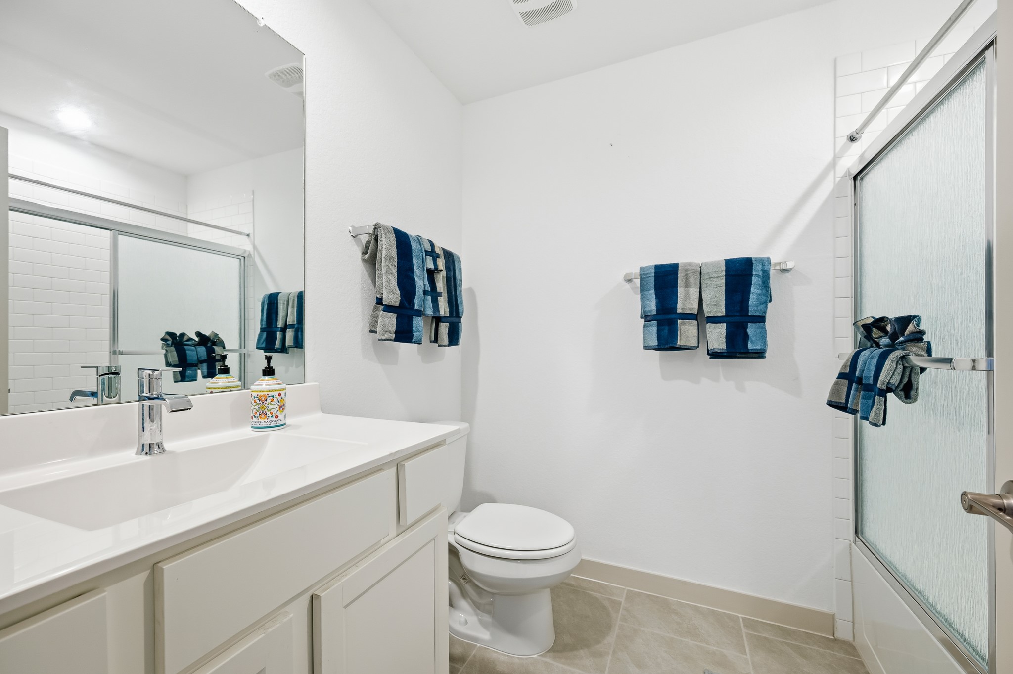 This bathroom features a sleek design with a large mirror, a modern vanity, and a glass-enclosed shower. The space is accented with blue and gray towels, creating a clean and inviting atmosphere.