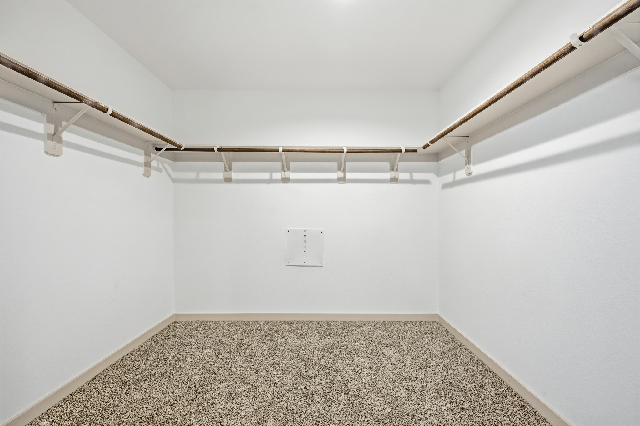 Spacious walk-in closet with carpeted flooring, white walls, and multiple wooden hanging rods for ample storage.