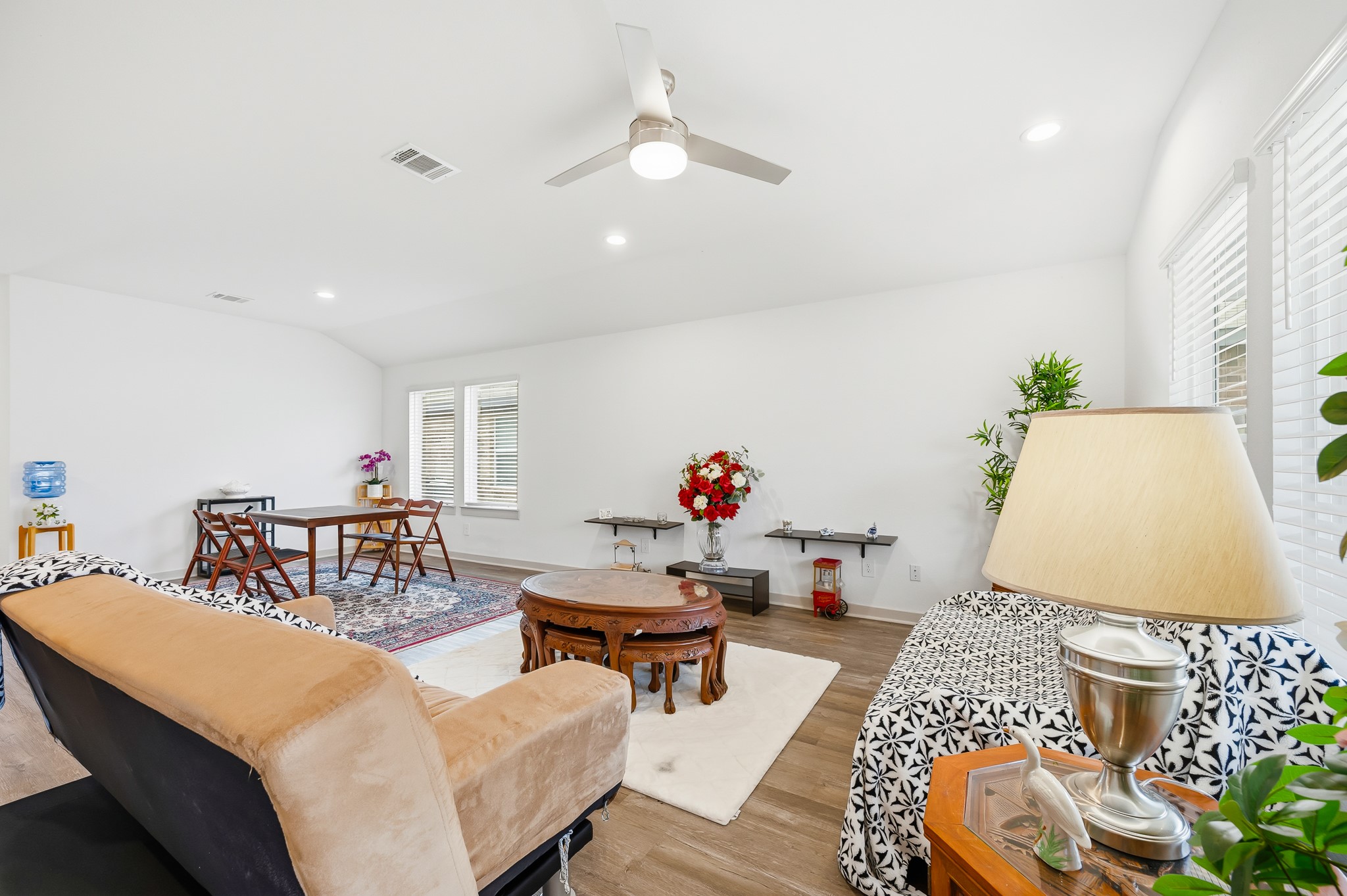 Bright and spacious living area with modern ceiling fan, hardwood floors, and ample natural light from large windows. The room features a comfortable seating arrangement, decorative plants, and a stylish coffee table, creating a welcoming atmosphere.