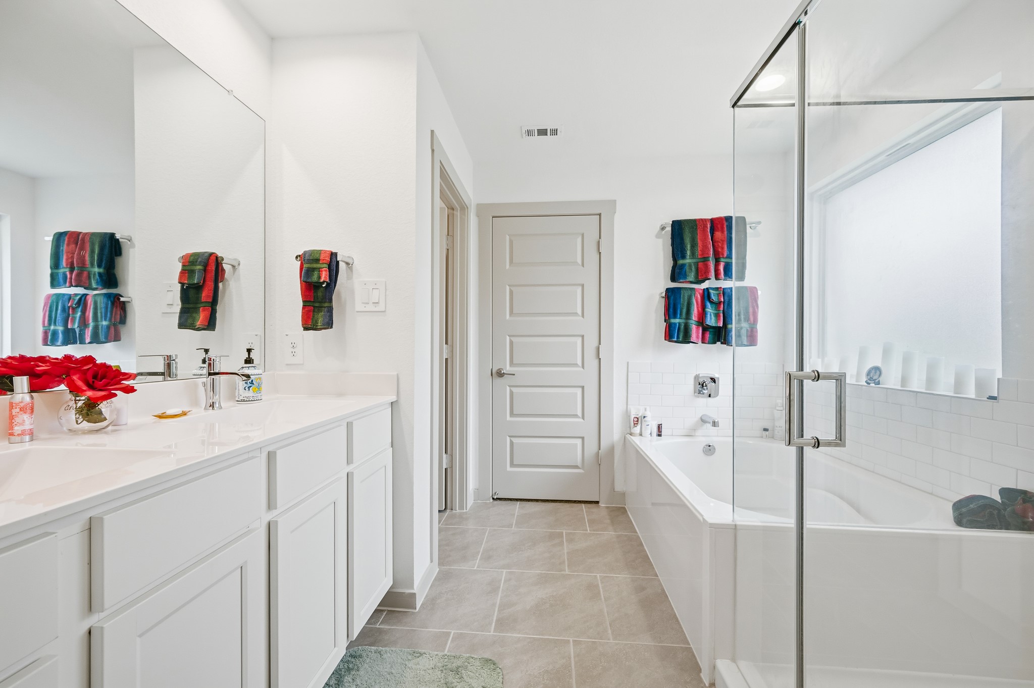 This modern bathroom features a spacious layout with a glass-enclosed shower, a luxurious bathtub, and a double vanity with ample storage. The bright, neutral palette is complemented by colorful towels, creating a welcoming and stylish atmosphere.