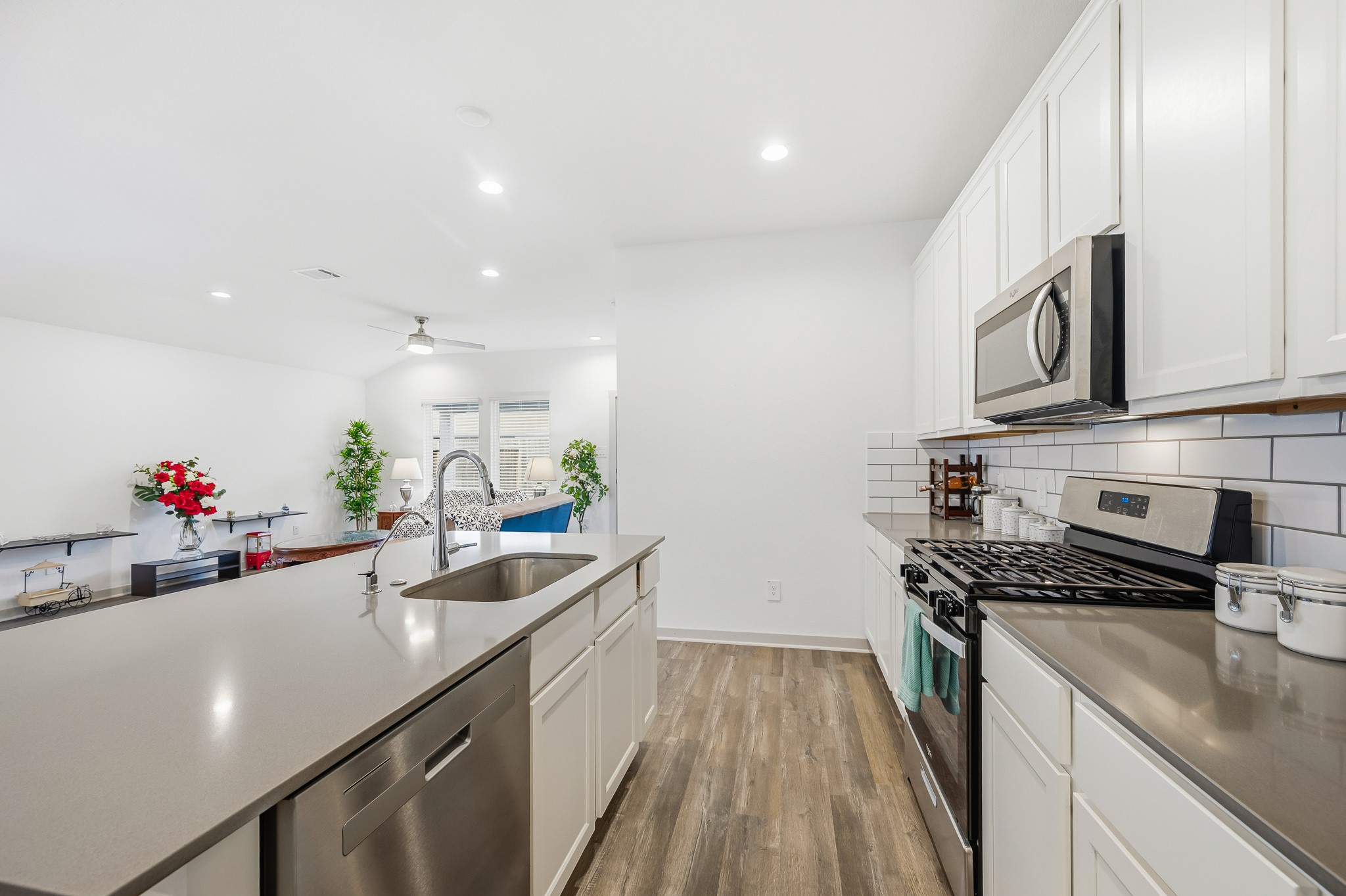 This modern kitchen features sleek stainless steel appliances, white cabinetry, and a spacious island with a built-in sink. The open layout connects seamlessly to a bright living area with wood-style flooring, creating an inviting space for entertaining.