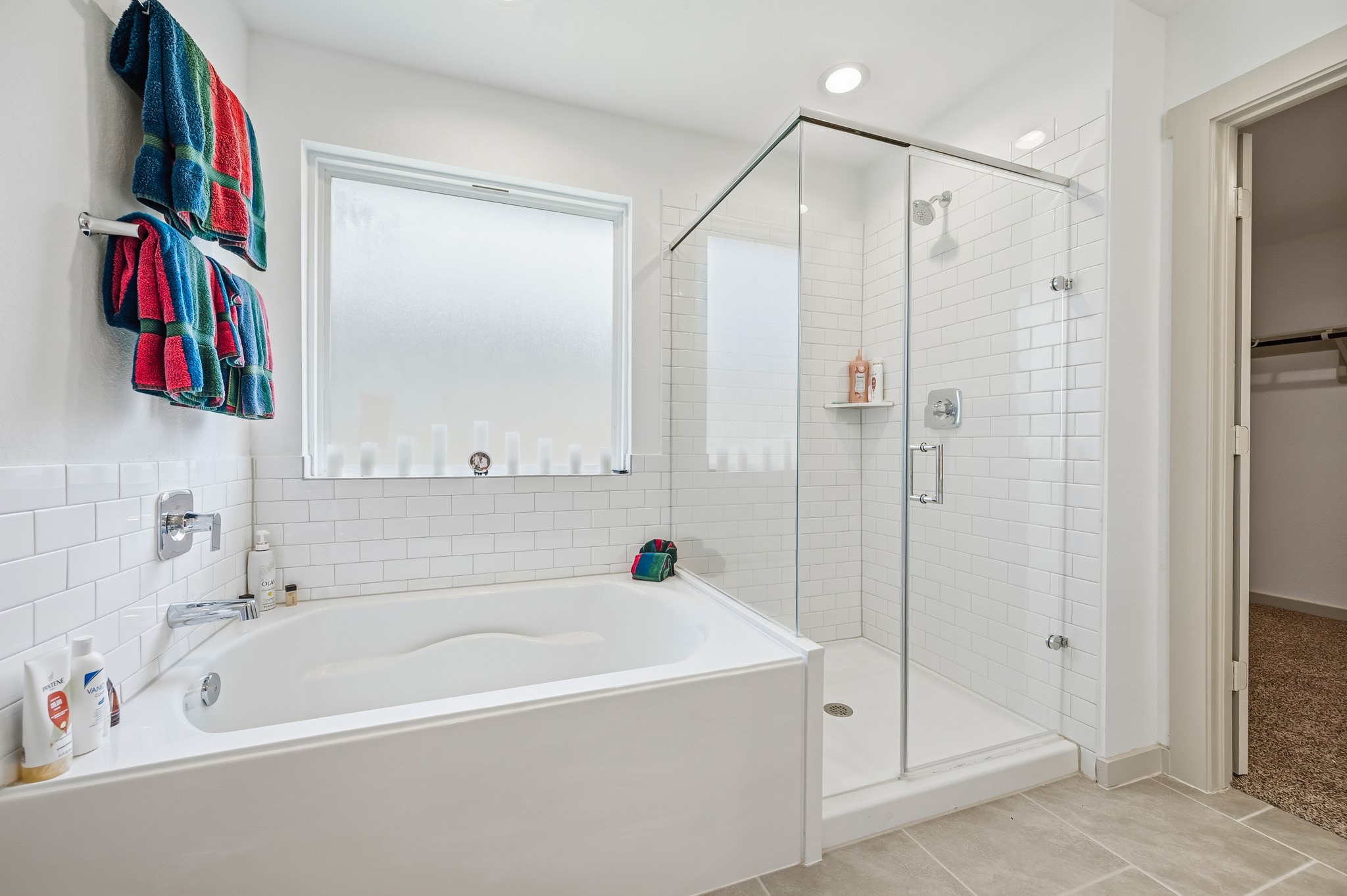 This modern bathroom features a sleek glass-enclosed shower, a spacious bathtub, and a large frosted window for natural light. The white subway tiles and neutral flooring create a clean, inviting atmosphere.
