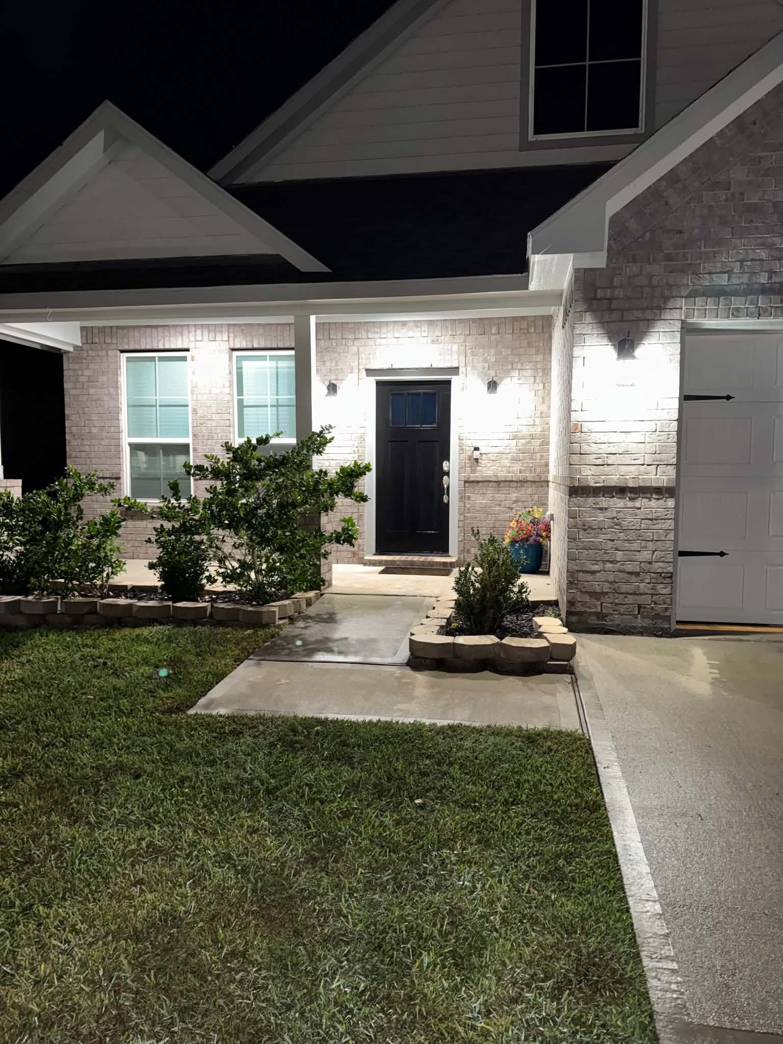 Charming home with a welcoming front porch, elegant black door, and beautifully lit exterior. The landscaped pathway leads to a well-maintained lawn, enhancing curb appeal.