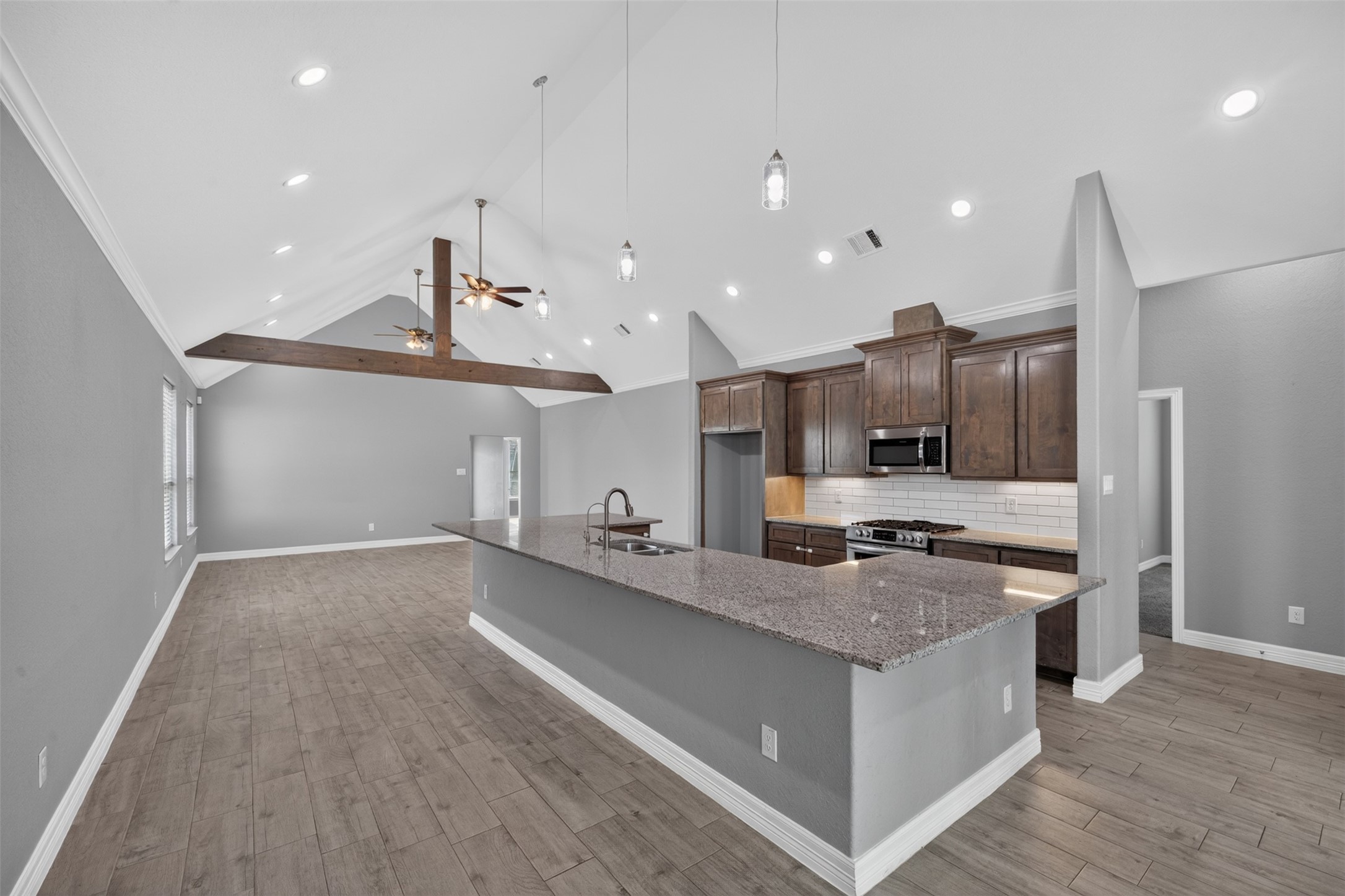 Spacious open-concept kitchen and living area featuring high vaulted ceilings with exposed wooden beams, modern fixtures, and elegant dark wood cabinetry.