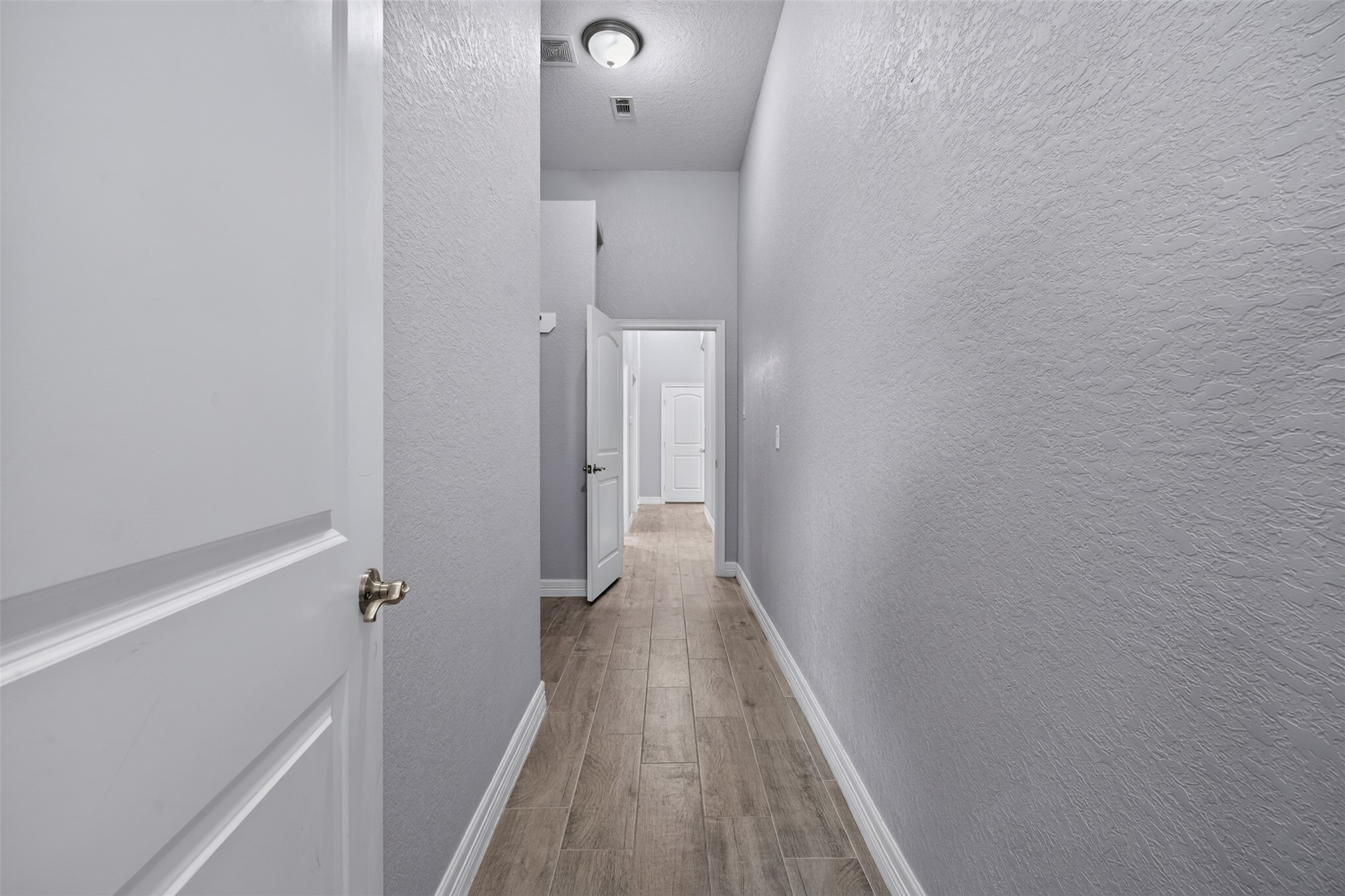 Bright and spacious hallway with elegant textured walls and sleek wood flooring, leading to multiple rooms.