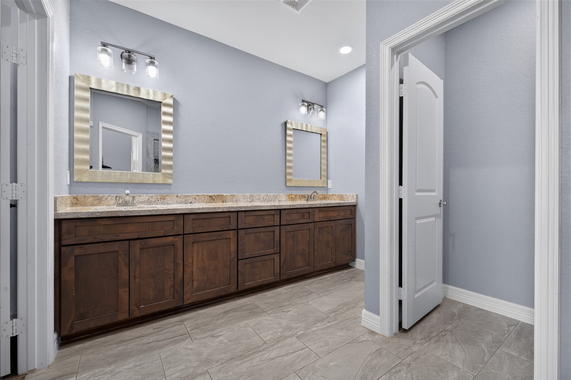 Elegant bathroom featuring a spacious double vanity with rich wood cabinetry, sleek countertops, and modern lighting, complemented by stylish tile flooring and a soothing color palette.