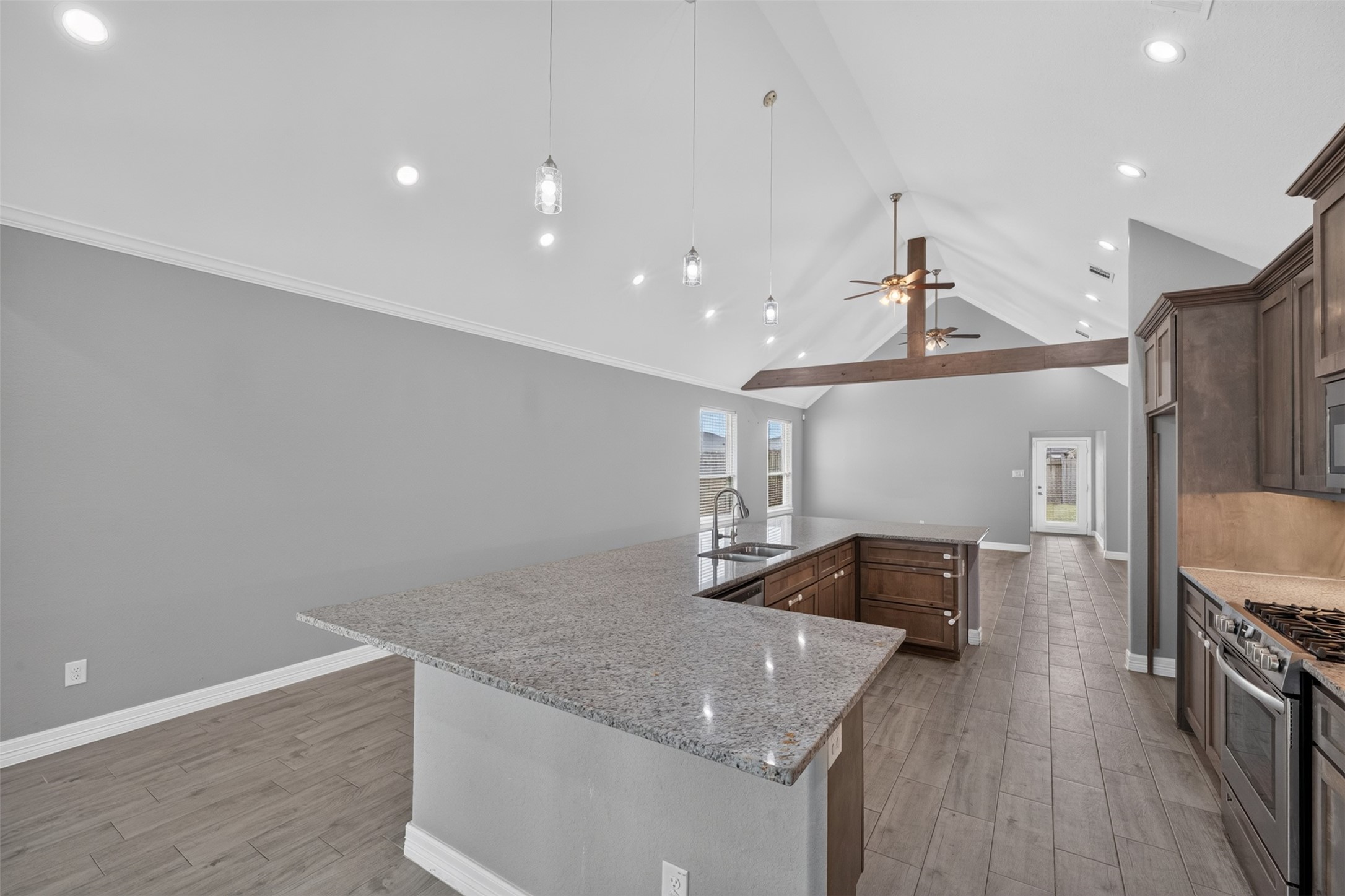 Spacious kitchen featuring high vaulted ceilings, modern pendant lighting, and a large granite island with ample seating. Stunning wood cabinetry complements the stainless steel appliances, while the open layout leads seamlessly into a bright living area.