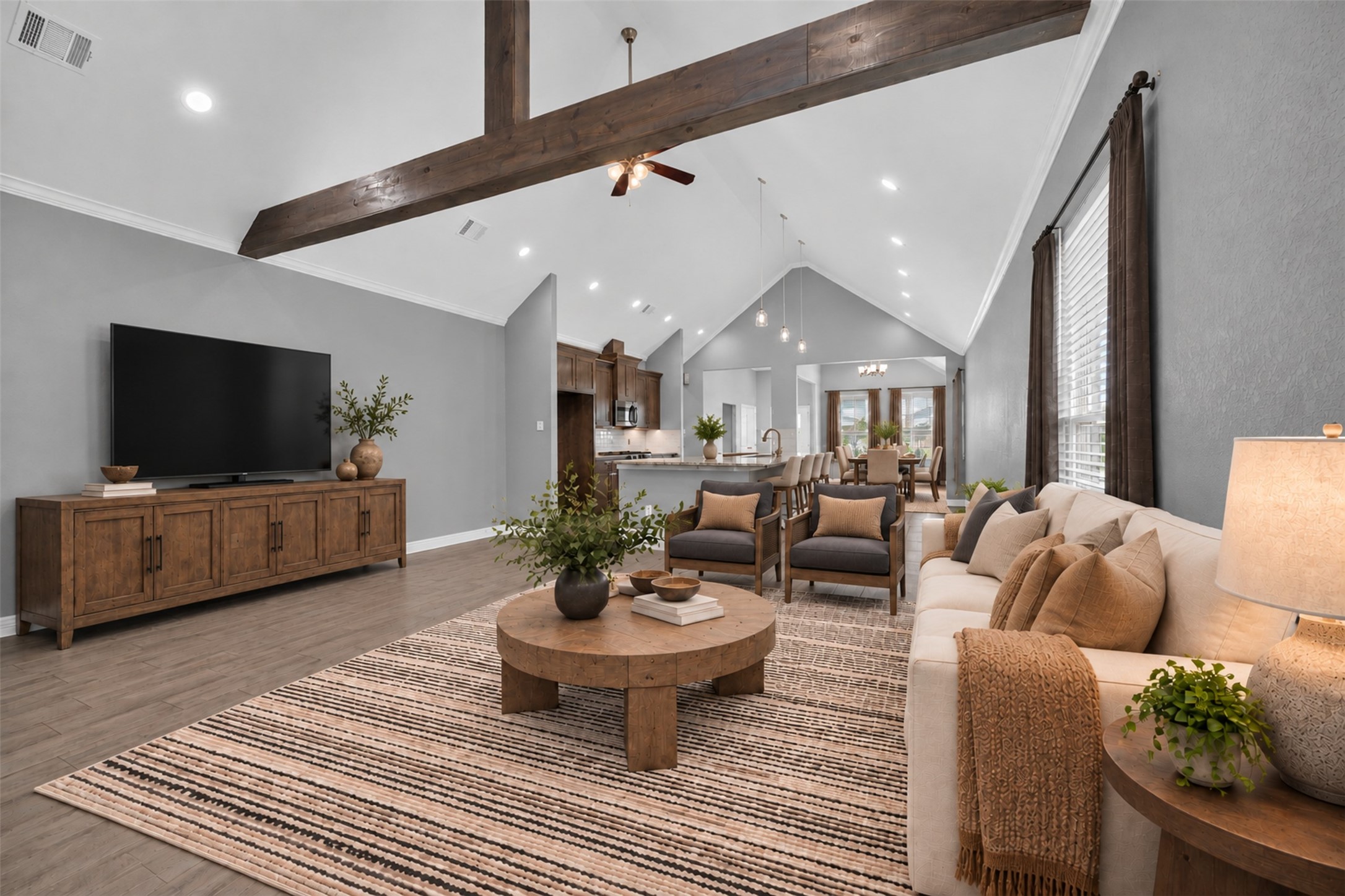 Stunning open-concept living area featuring vaulted ceilings with exposed wood beams, a cozy seating arrangement, and a seamless flow into the dining and kitchen spaces, perfect for entertaining.