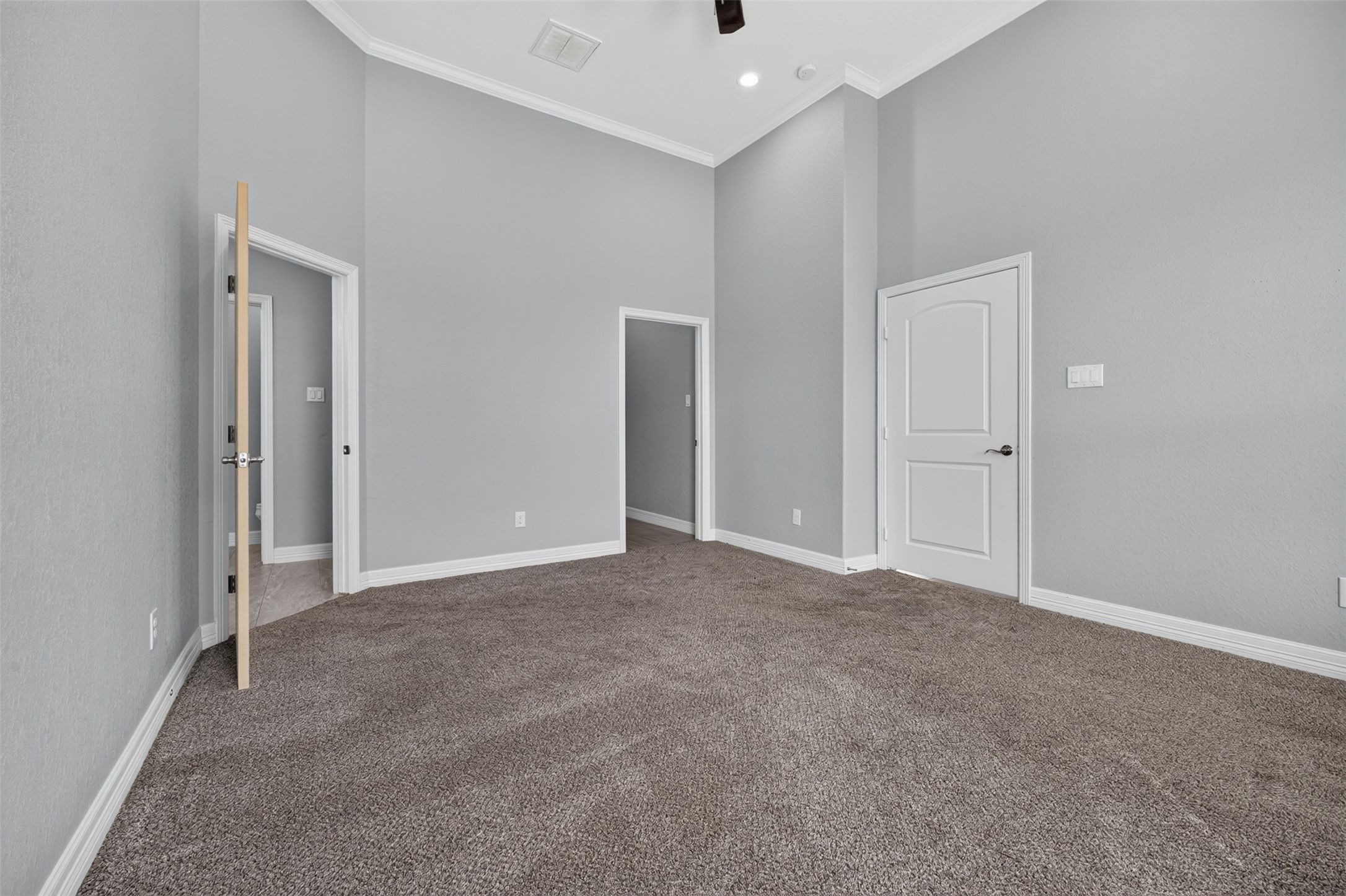Spacious room with high ceilings, soft carpet, and neutral gray walls, featuring elegant white trim and multiple doorways for convenient access.