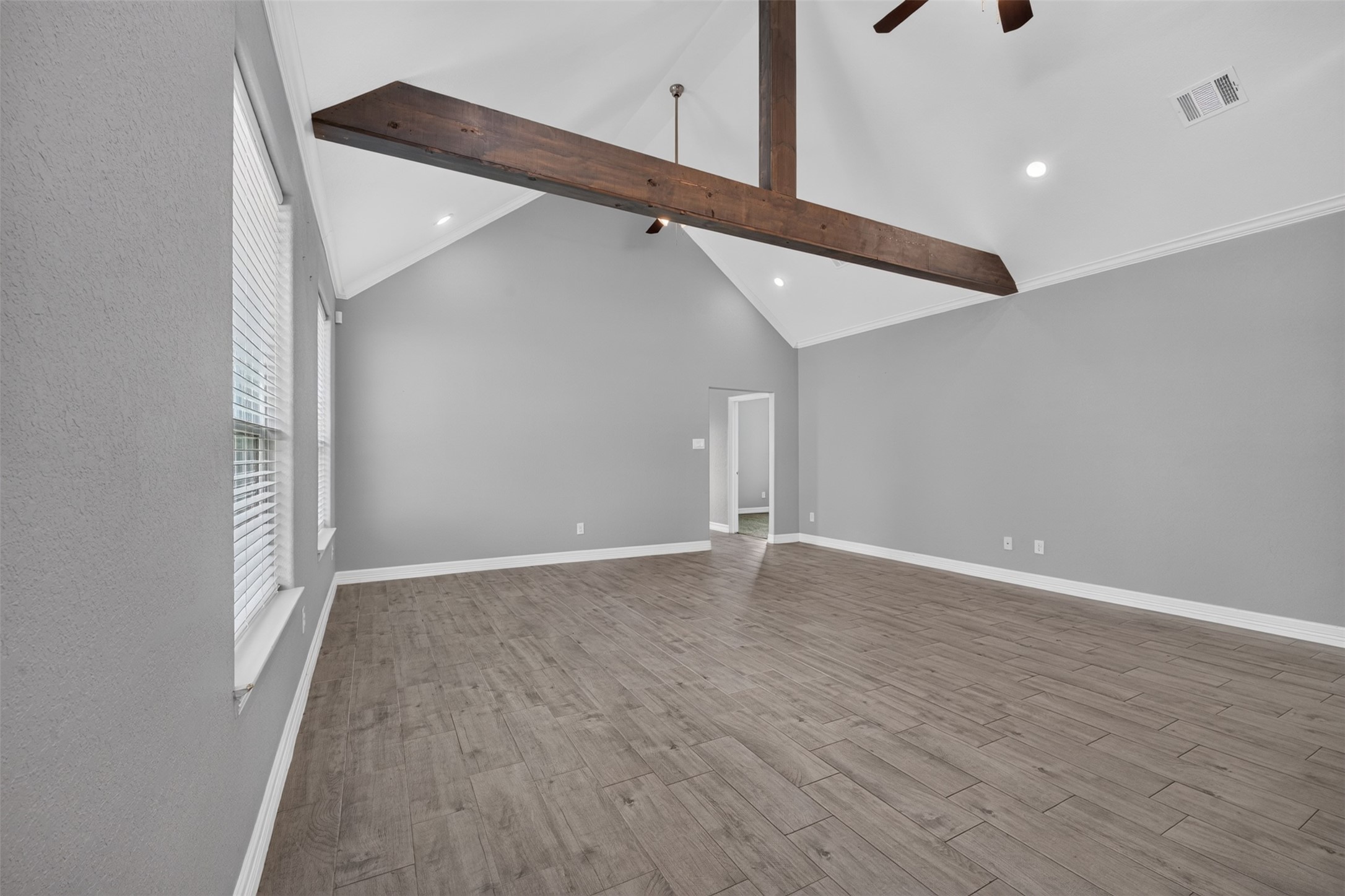 Spacious living area featuring high vaulted ceilings with a striking wooden beam and elegant wood-look tile flooring, perfect for modern living.