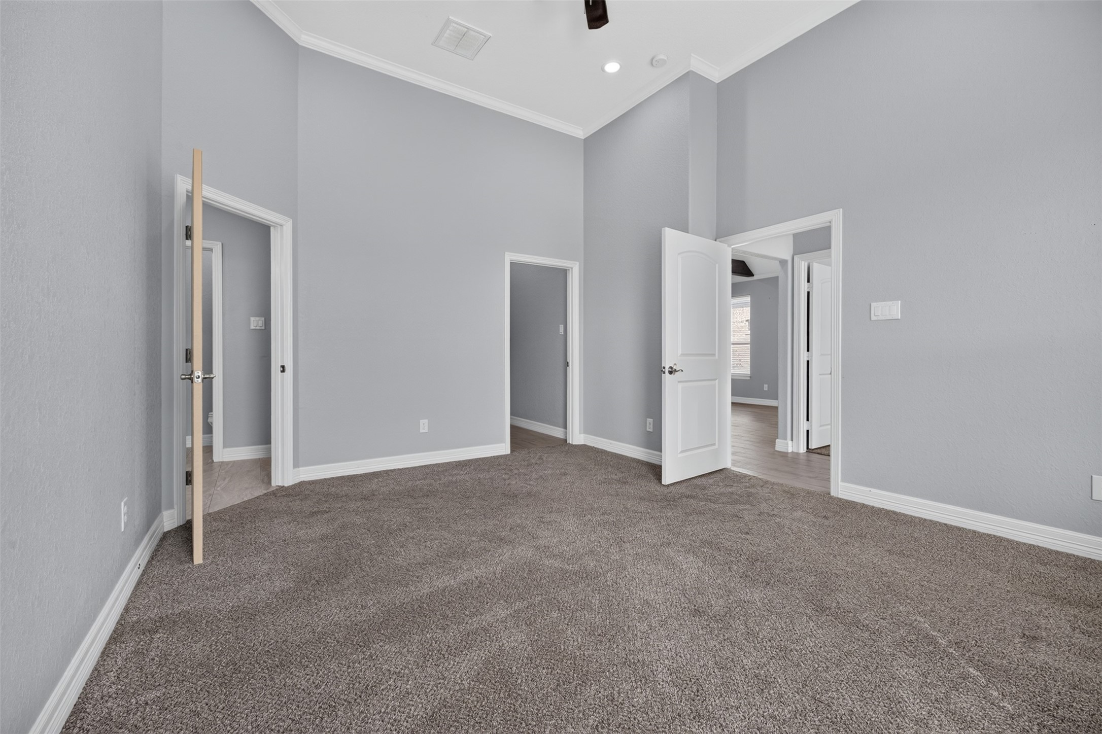 Spacious bedroom with high ceilings, neutral gray walls, and plush carpeting, offering multiple entryways for versatile access.