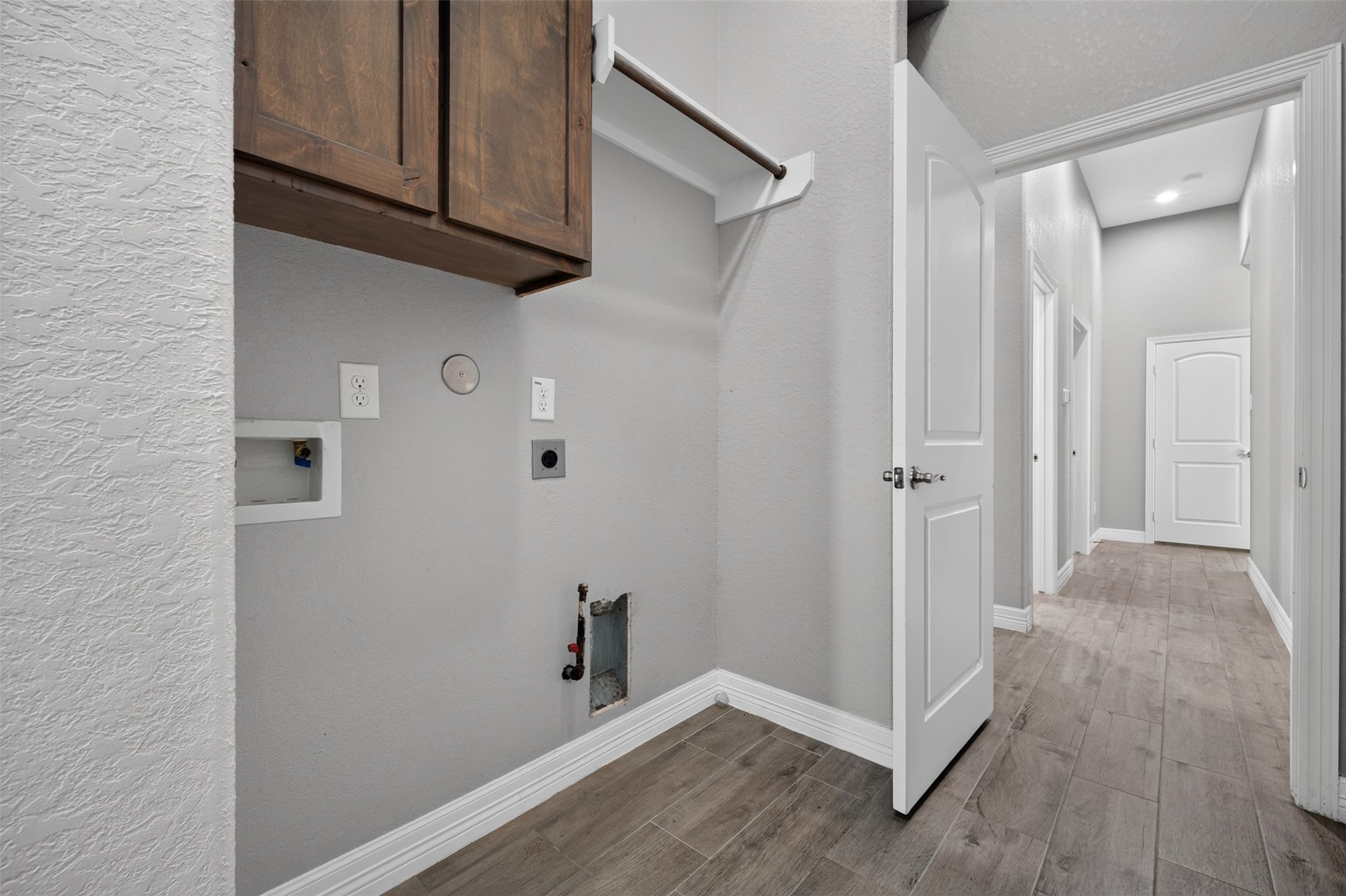 Spacious laundry area with built-in wooden cabinets and connections for washer and dryer, leading to a bright hallway with elegant tile flooring.