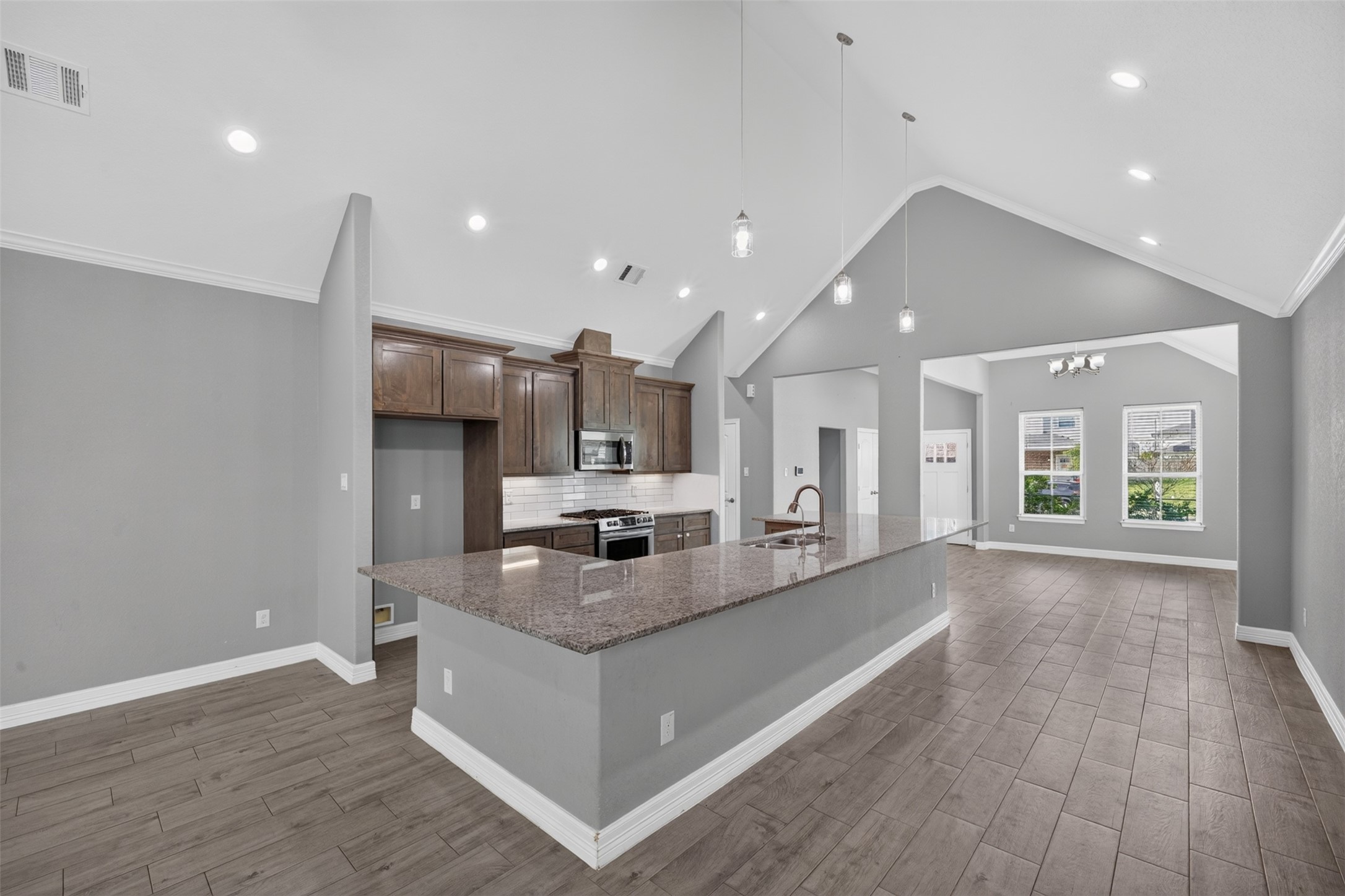 Spacious open-concept kitchen and living area featuring high vaulted ceilings, modern lighting, and a large granite island with ample seating.