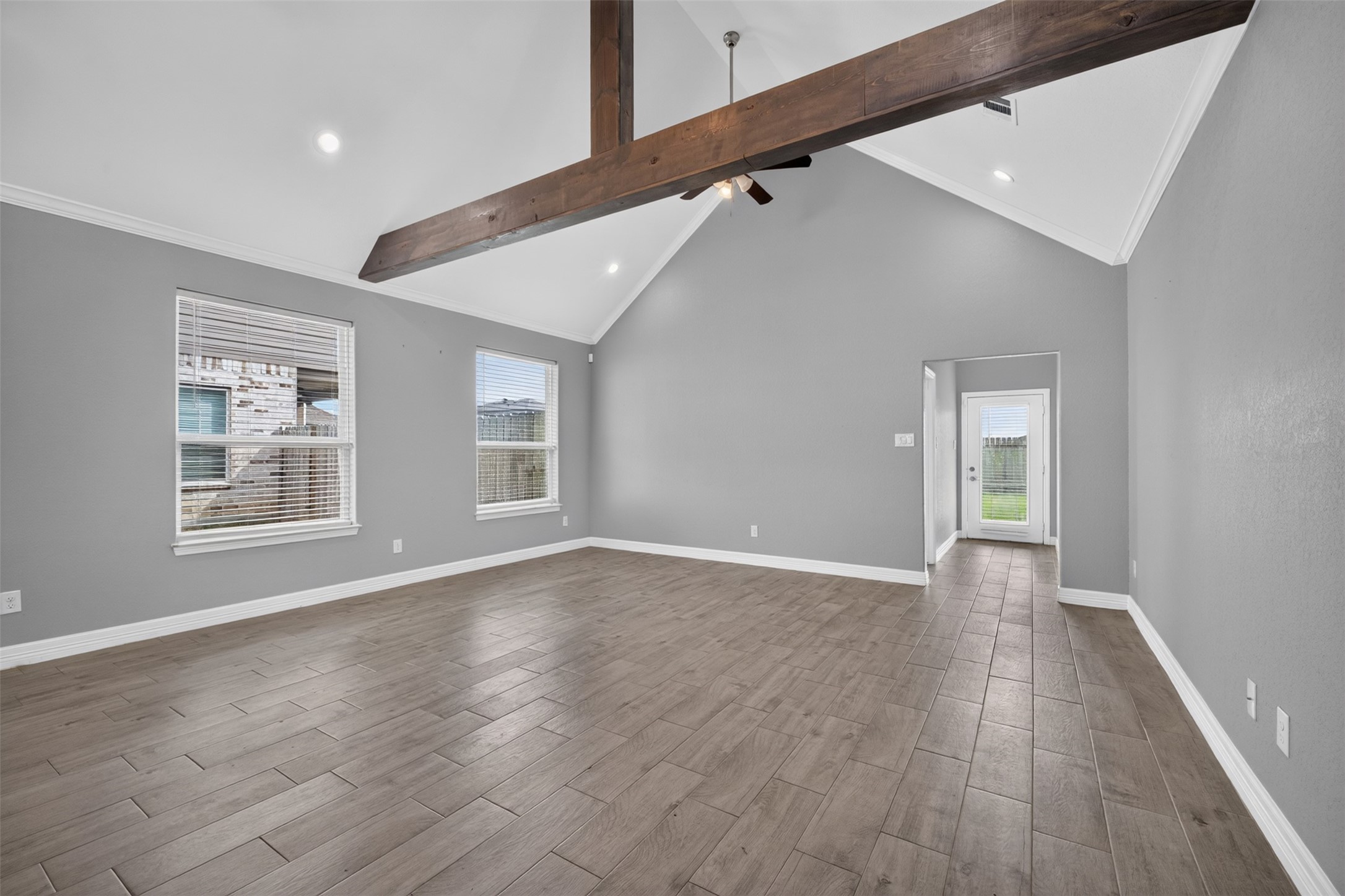 Spacious living area featuring high vaulted ceilings with exposed wooden beams, elegant tile flooring, and abundant natural light from large windows.