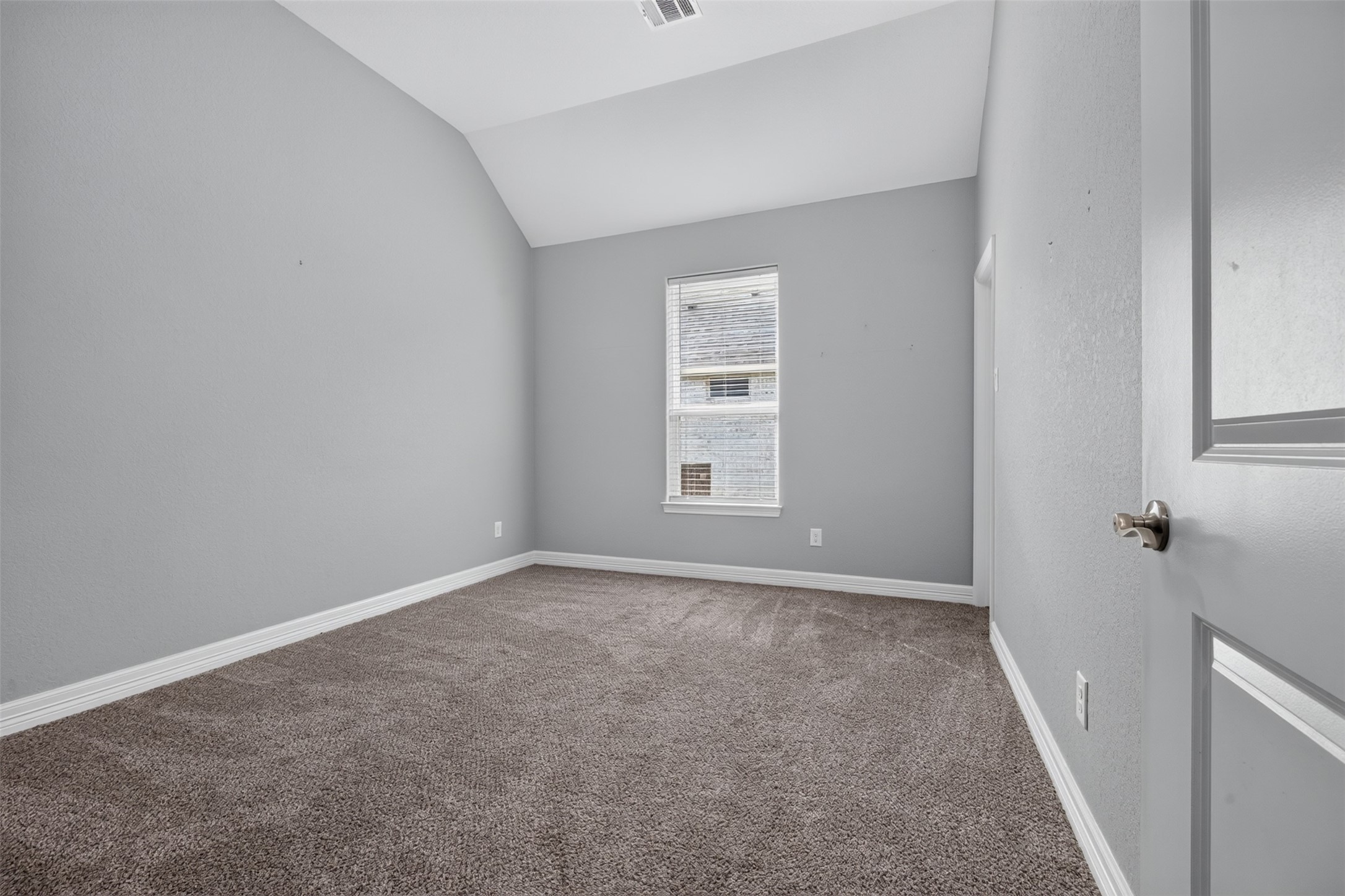 Cozy bedroom with soft carpeting, a neutral gray color palette, and a vaulted ceiling, offering a tranquil retreat.