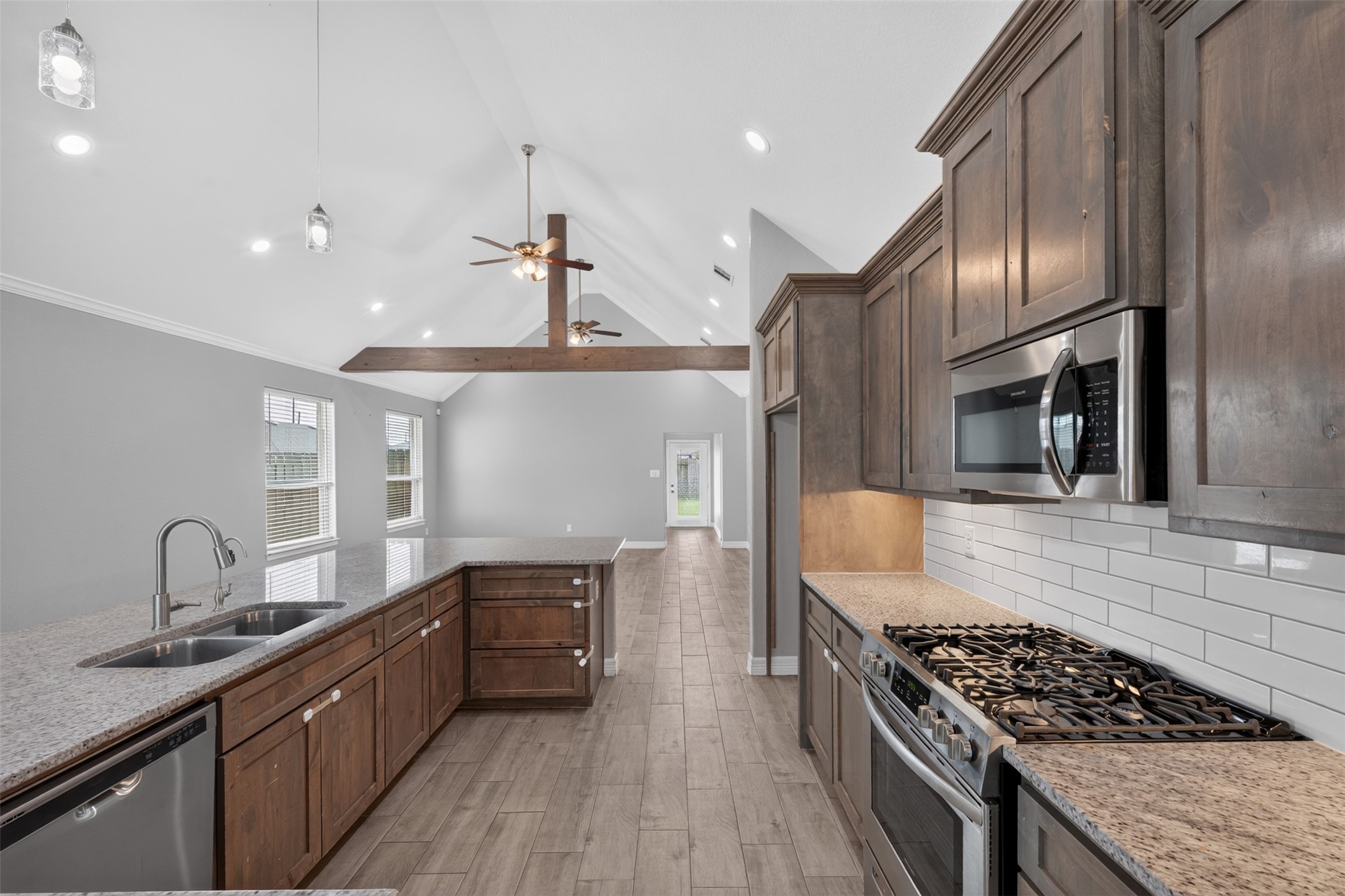 Spacious modern kitchen with elegant wood cabinetry, granite countertops, and stainless steel appliances, seamlessly flowing into an open living area with vaulted ceilings and abundant natural light.