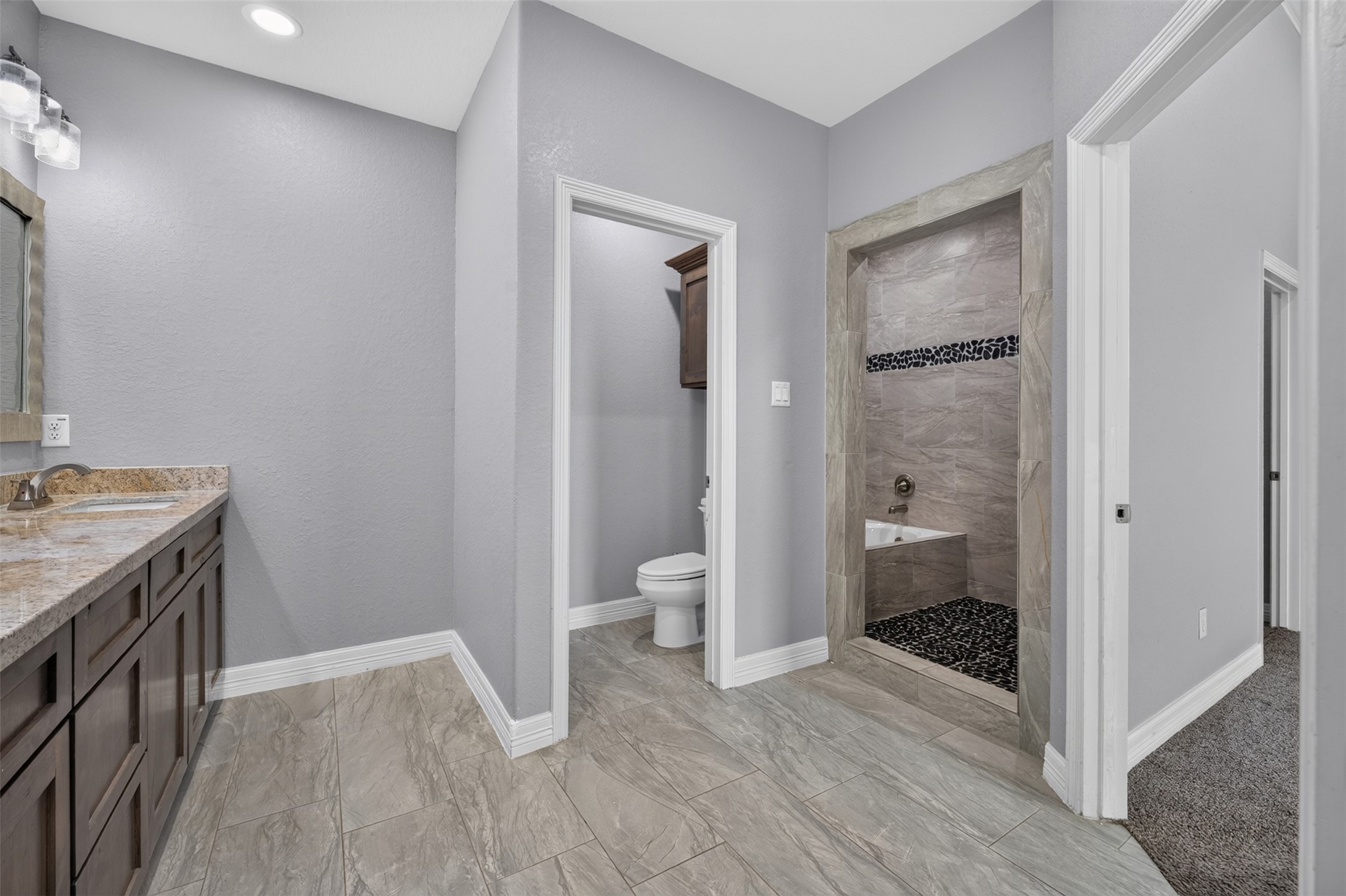 Spacious bathroom featuring elegant tile flooring, a dual-sink vanity with granite countertops, and a modern walk-in shower with stylish tile accents.