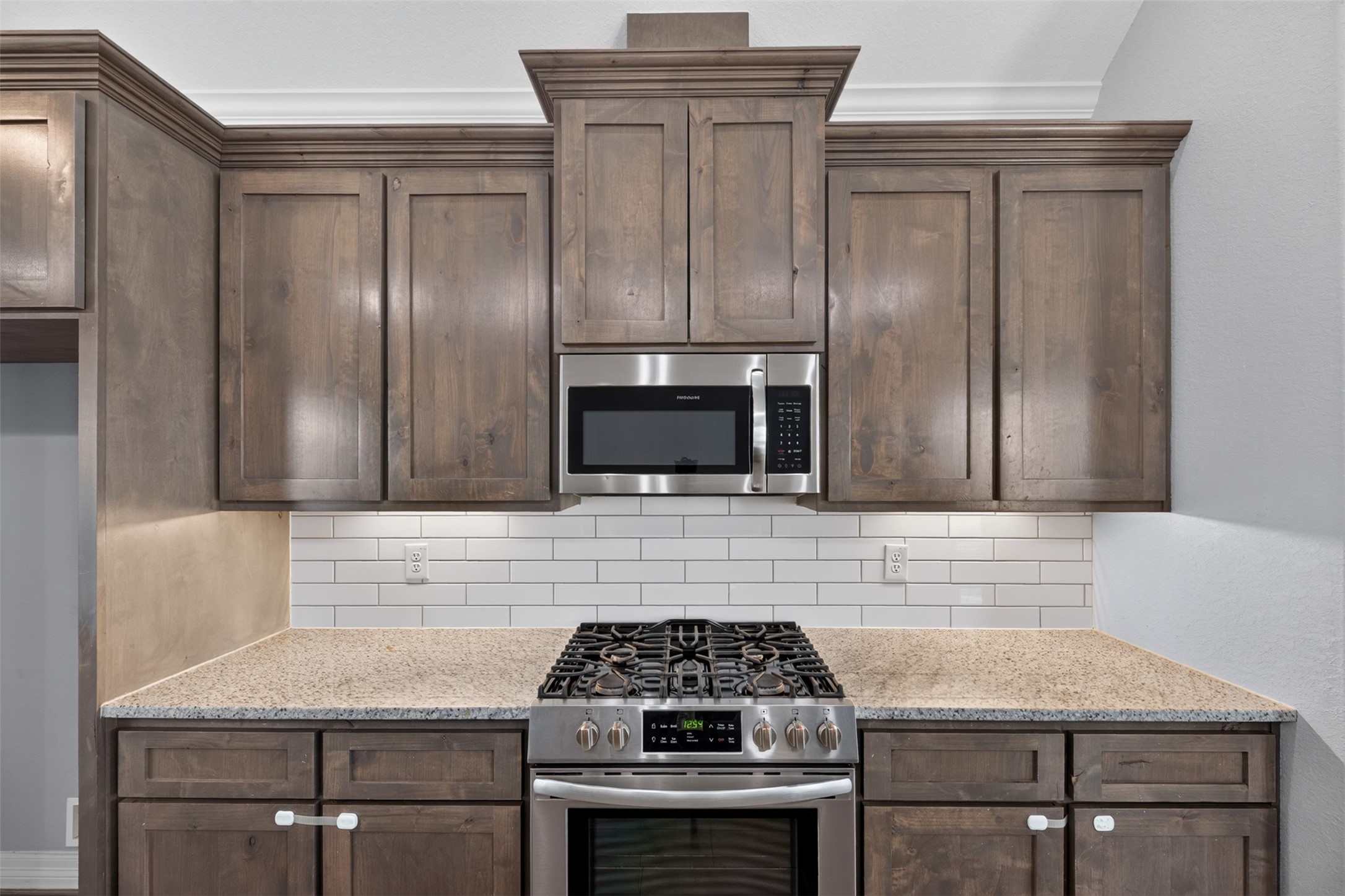 Elegant kitchen featuring rich wood cabinetry, sleek granite countertops, and a modern stainless-steel stove with a built-in microwave, all complemented by a classic white subway tile backsplash.