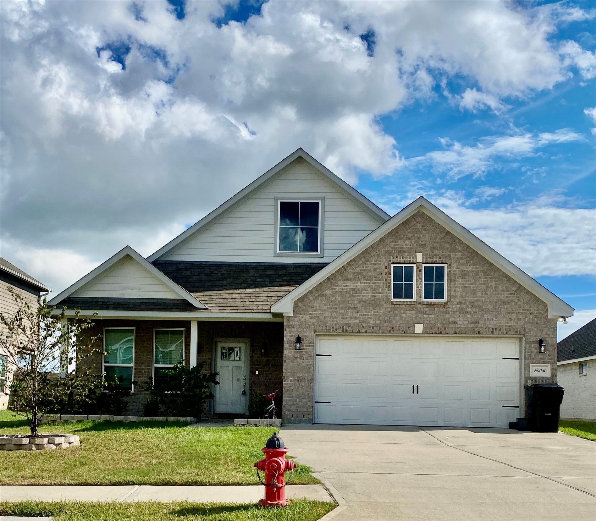 Charming brick home with a spacious two-car garage and inviting front porch, set against a backdrop of blue skies and lush greenery.