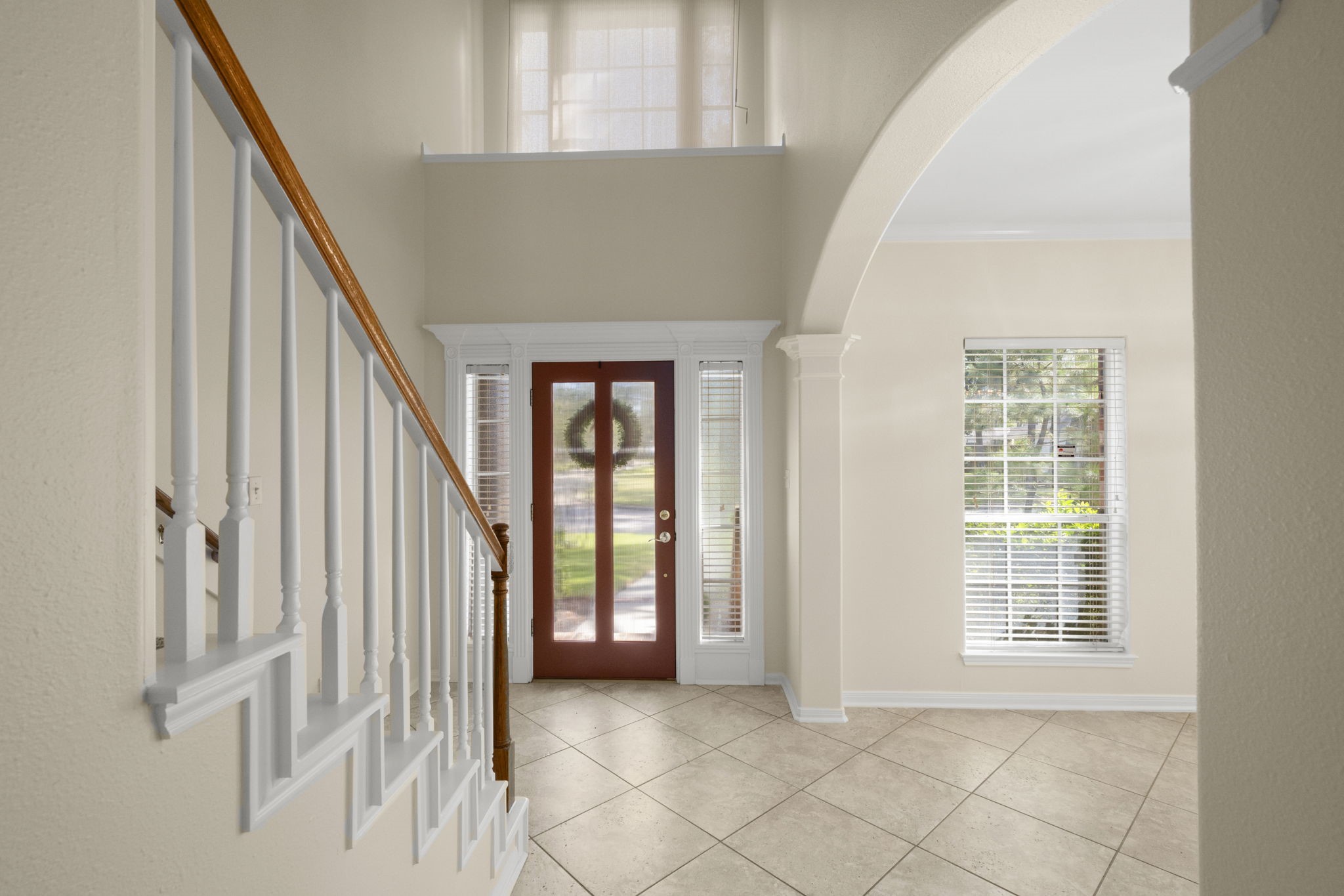 SOARING CEILINGS & TIMELESS ARCHITECTURAL CHARM! This impressive 19-foot, two-story foyer makes a grand first impression with abundant natural light pouring through the elevated window and flanking sidelights. A decorative display ledge, graceful arched opening, elegant staircase with wood handrail, and easy-care tile flooring create a bright, welcoming entry filled with character!
