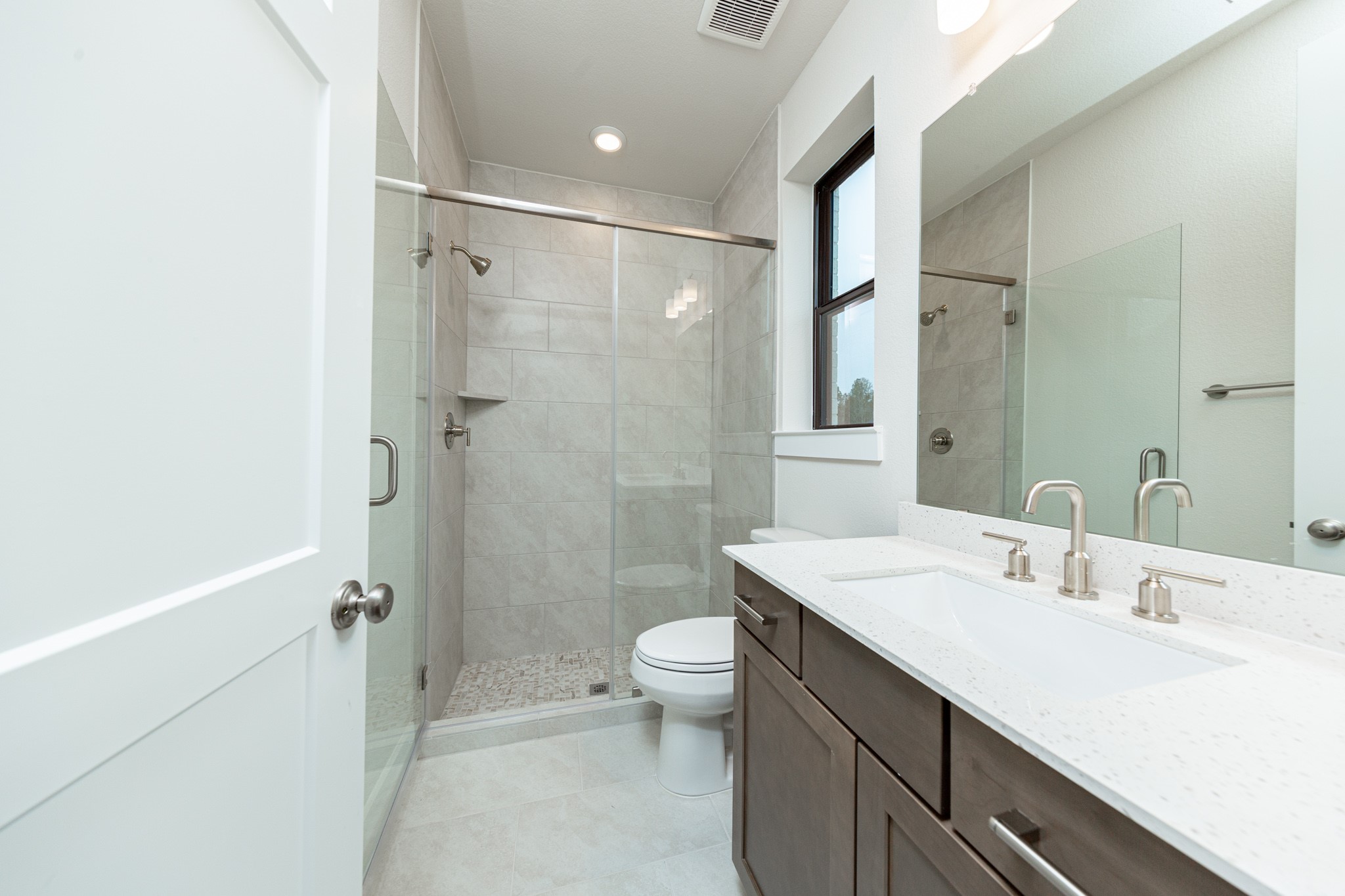 The private en suite bathroom features a modern white vanity with brushed nickel fixtures, mirror, lights, recessed lighting over the walk-in shower.