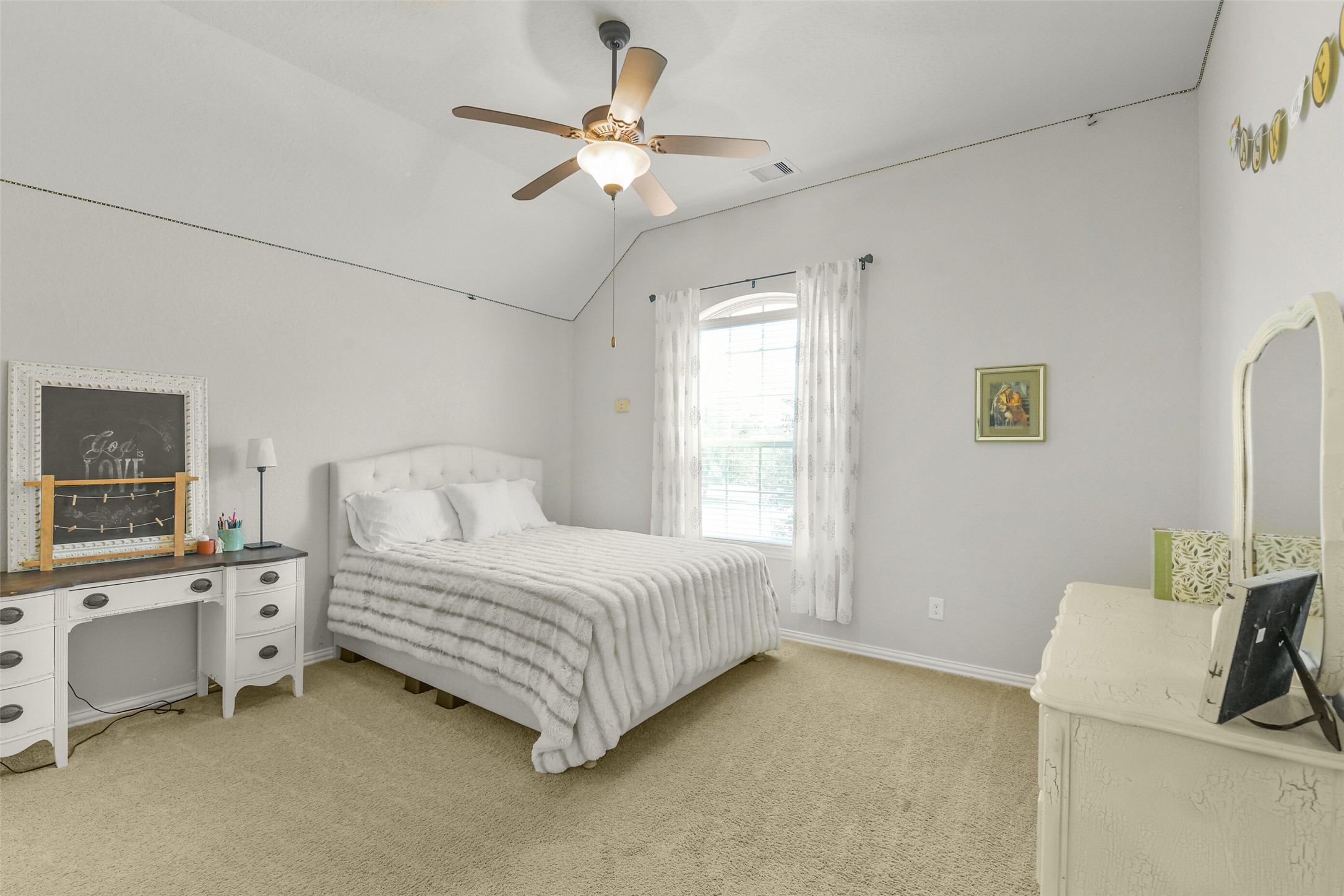 Comfortable secondary bedroom featuring a ceiling fan, natural light, and neutral carpeting.