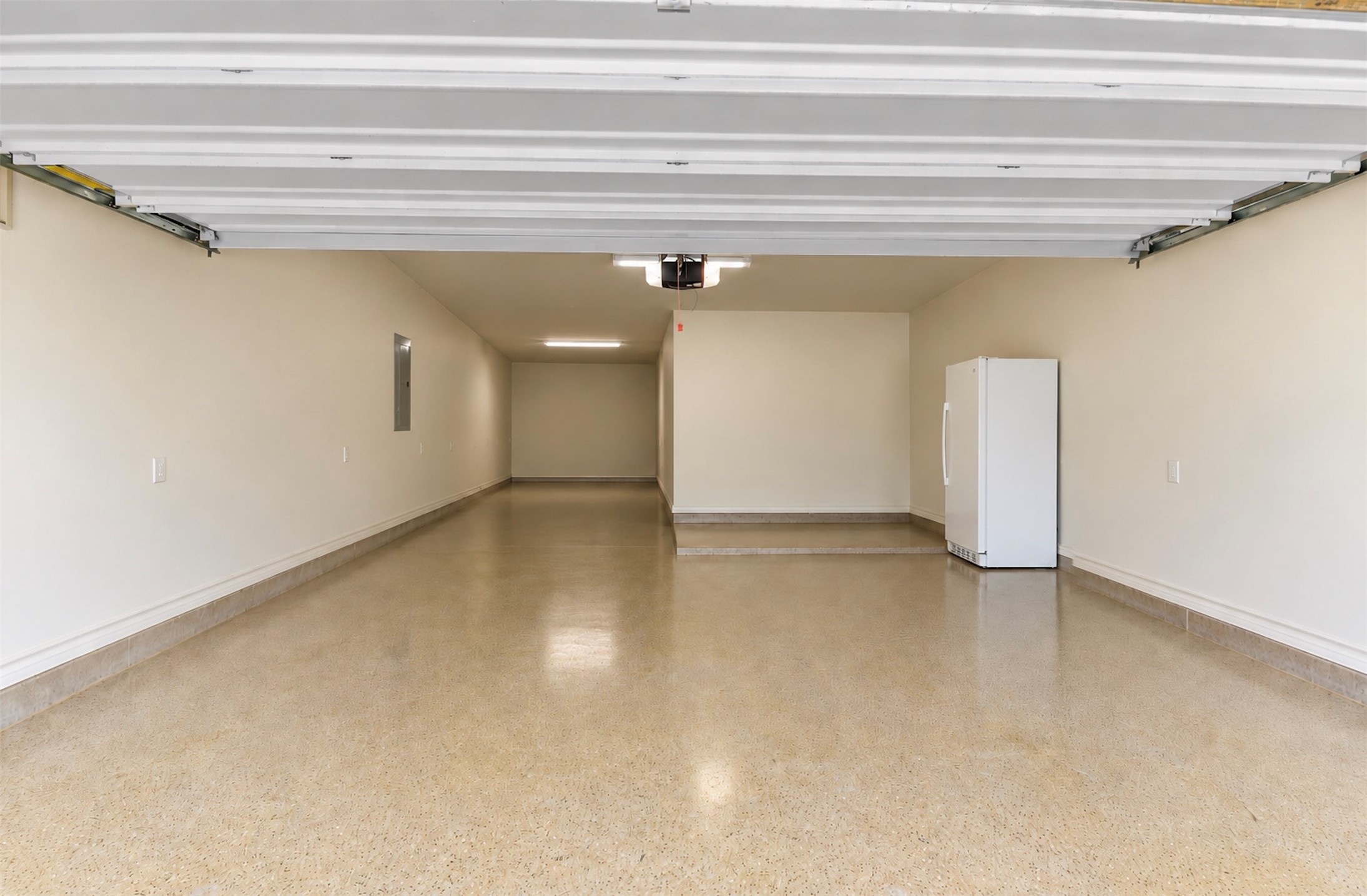 Spacious tandem garage with an extended parking or storage area and durable finished flooring. (Fridge in garage can stay). (AI Adjusted to show space)