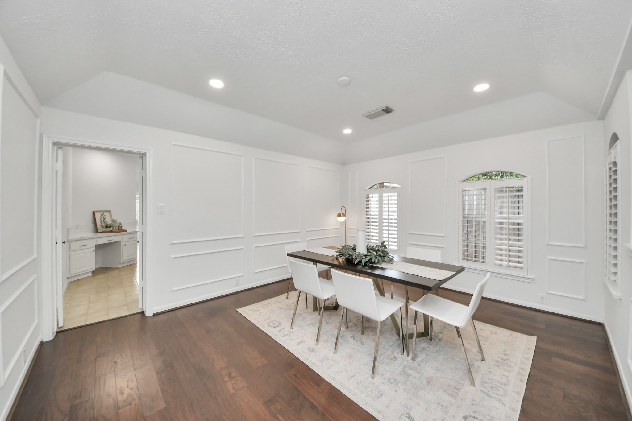A spacious dining room with wood floors, decorative wall molding, and plantation shutters. Located right off the kitchen for easy serving.