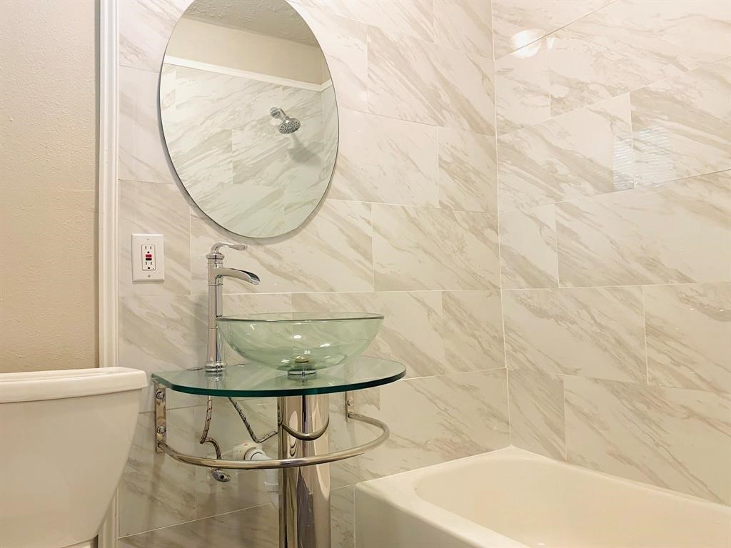 Chic bathroom featuring elegant marble-patterned tiles, a modern glass vessel sink, and a sleek round mirror for a luxurious touch.