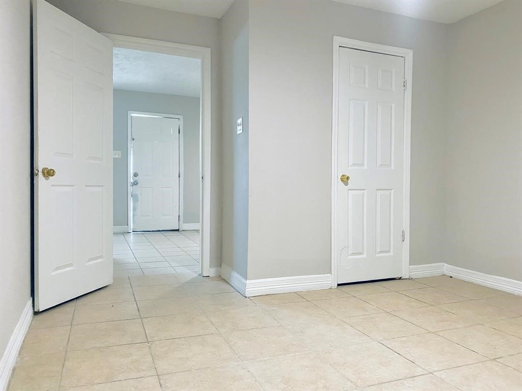 Bright, neutral-toned room with tiled flooring and multiple doorways, offering versatile space and easy access to adjoining areas.