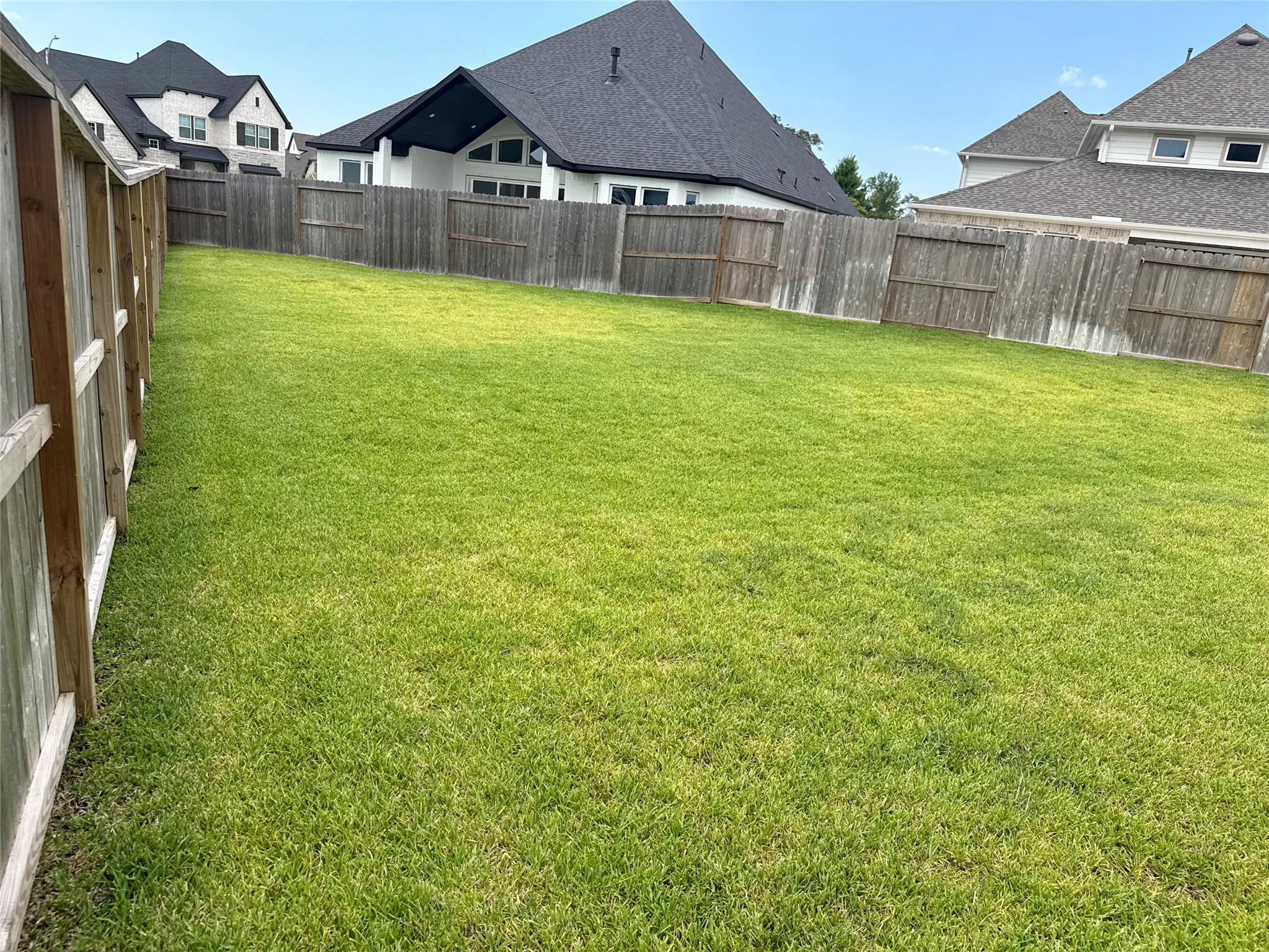 Expansive, well-maintained backyard with lush green grass, perfect for outdoor activities and entertaining, and a pool  enclosed by a sturdy wooden fence for privacy.