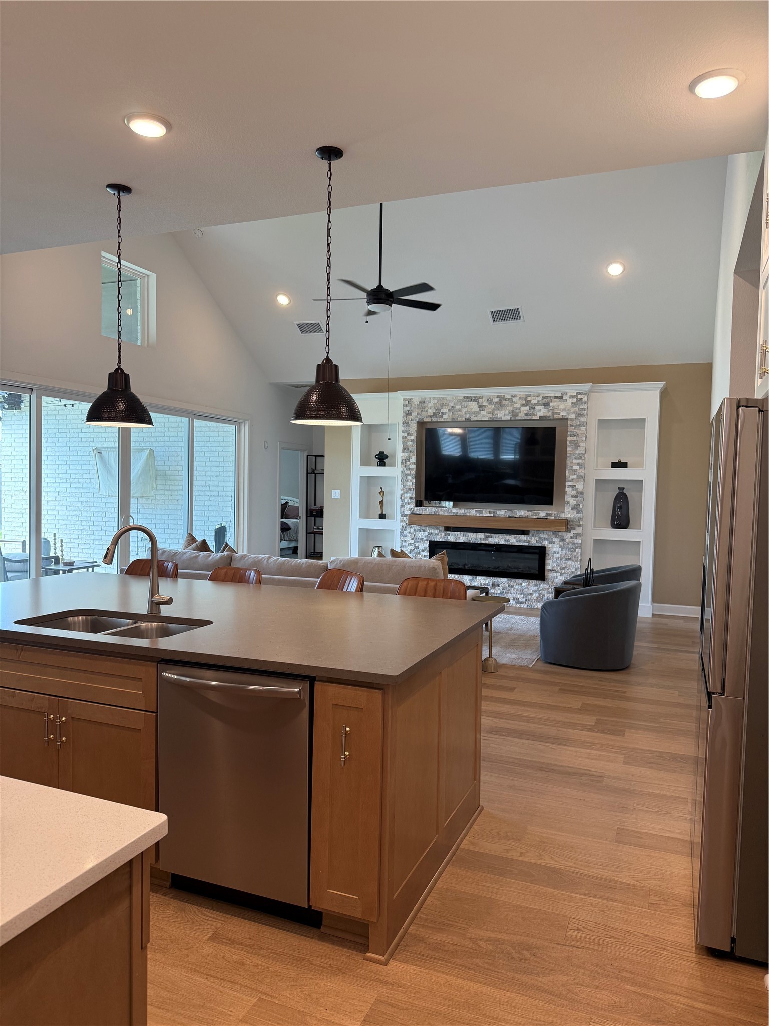 Spacious open-concept living area featuring a modern kitchen with a large island, sleek appliances, and stylish pendant lighting, seamlessly flowing into a cozy living room with a custom designed fireplace and built-in shelving.