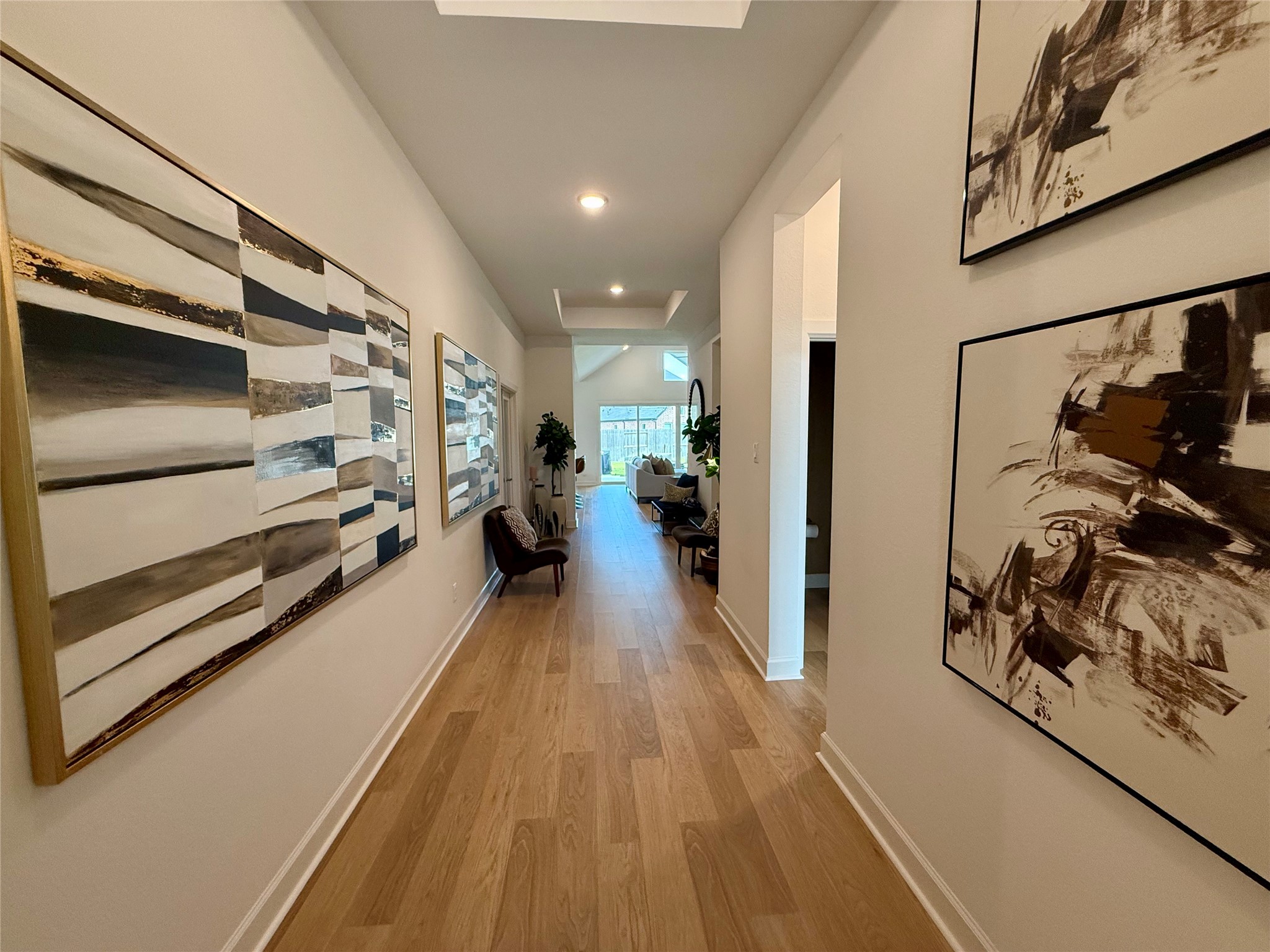 A welcoming hallway with elegant wooden flooring and modern abstract art leads to a bright, open living space, creating a stylish and inviting entrance. A welcoming hallway with elegant wooden flooring and modern abstract art leads to a bright, open living space, creating a stylish and inviting entrance.