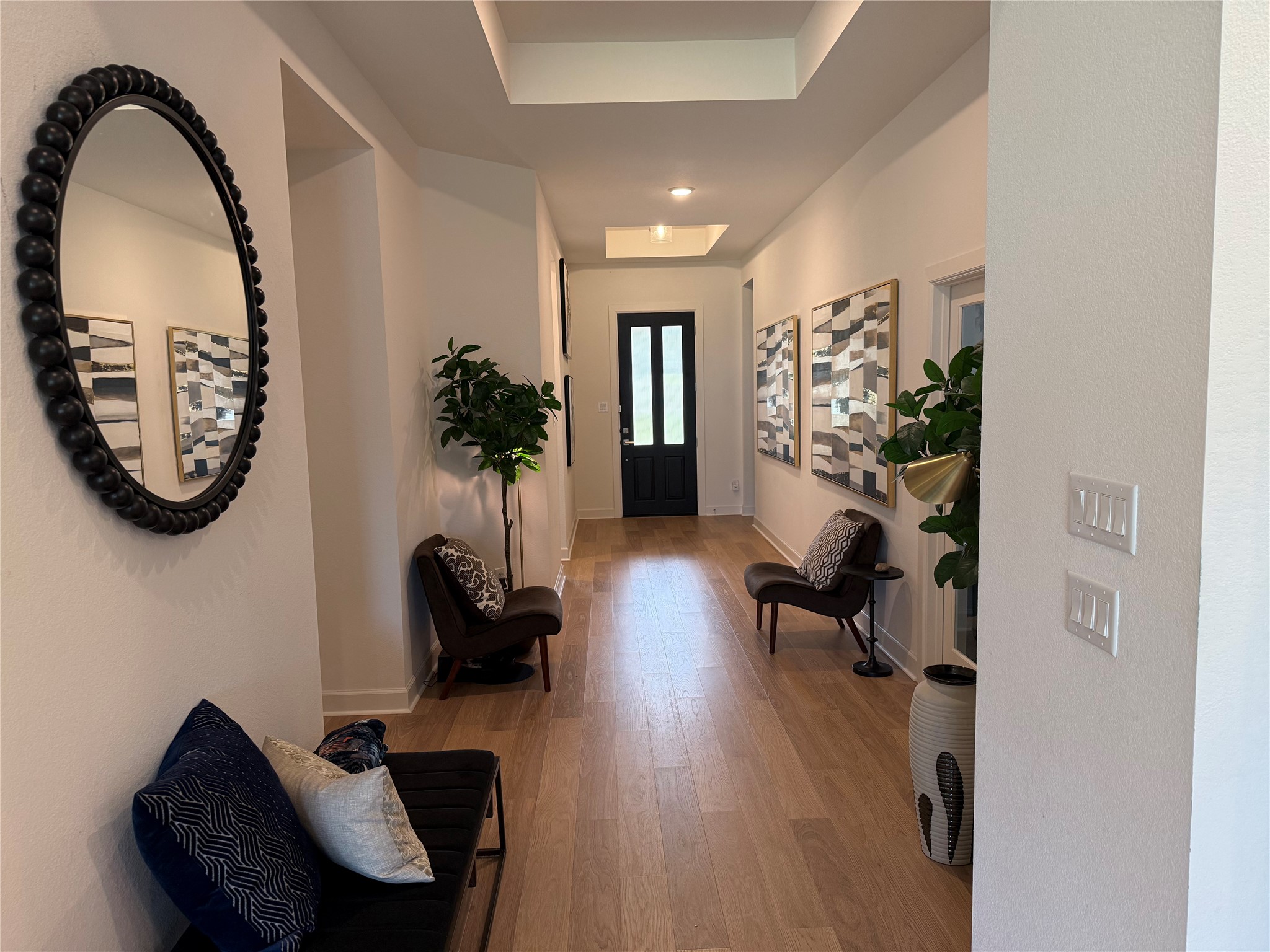 Elegant hallway with warm wood flooring, modern decor, and ample natural light leads to a striking black front door. Elegant hallway with warm wood flooring, modern decor, and ample natural light leads to a striking black front door.