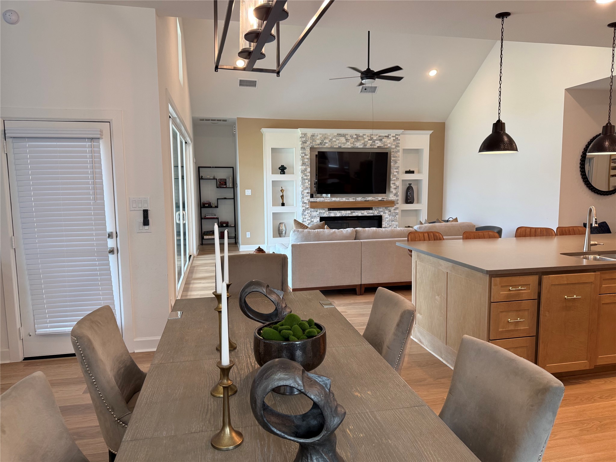 Spacious open-concept living area featuring a modern kitchen with pendant lighting, a cozy seating area, and a stylish custom designed  stone fireplace with built-in shelving and a mounted TV.