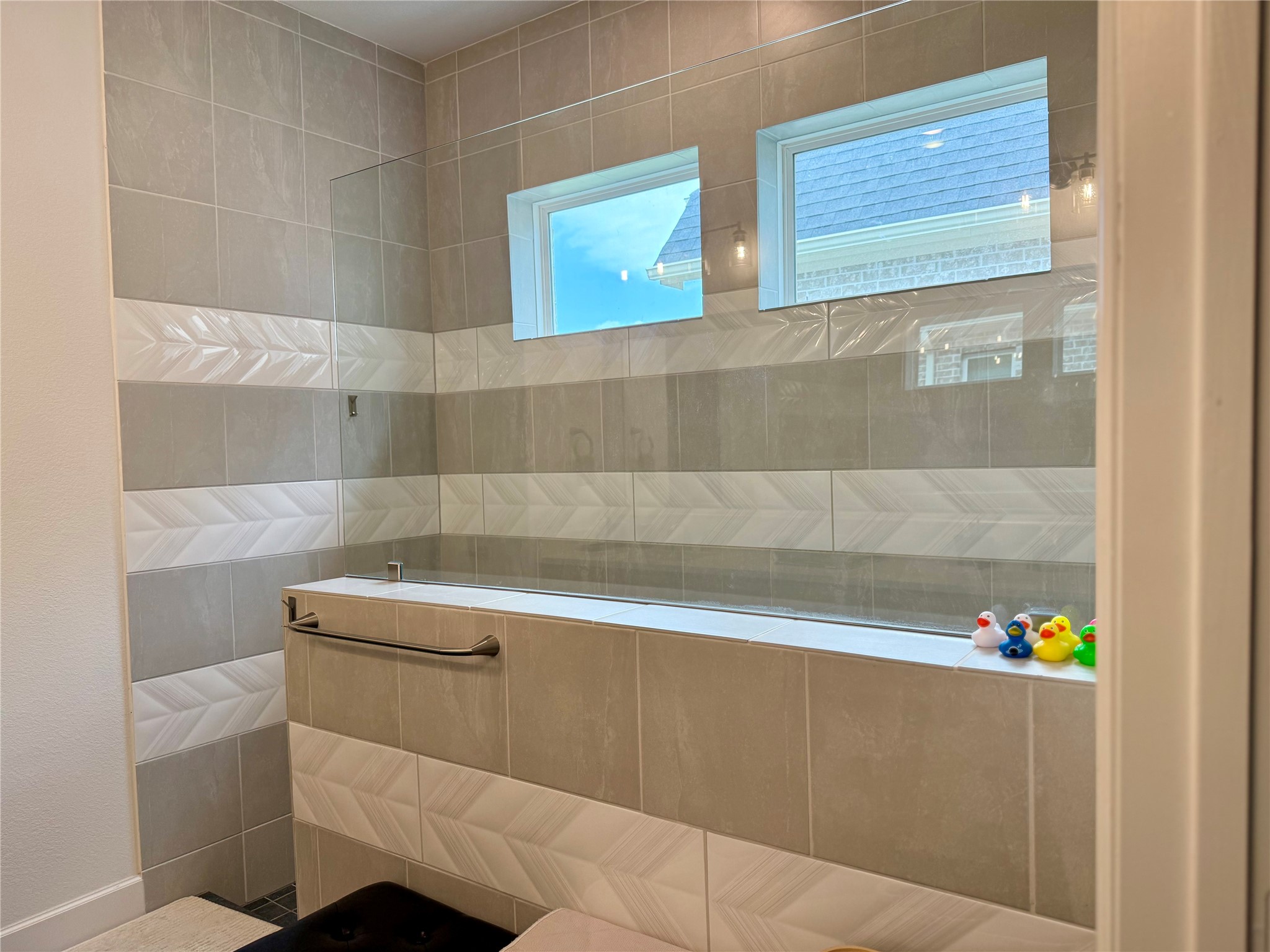 Elegant bathroom featuring a modern soaking tub with stylish tile surround and two bright windows, creating a serene and inviting atmosphere.