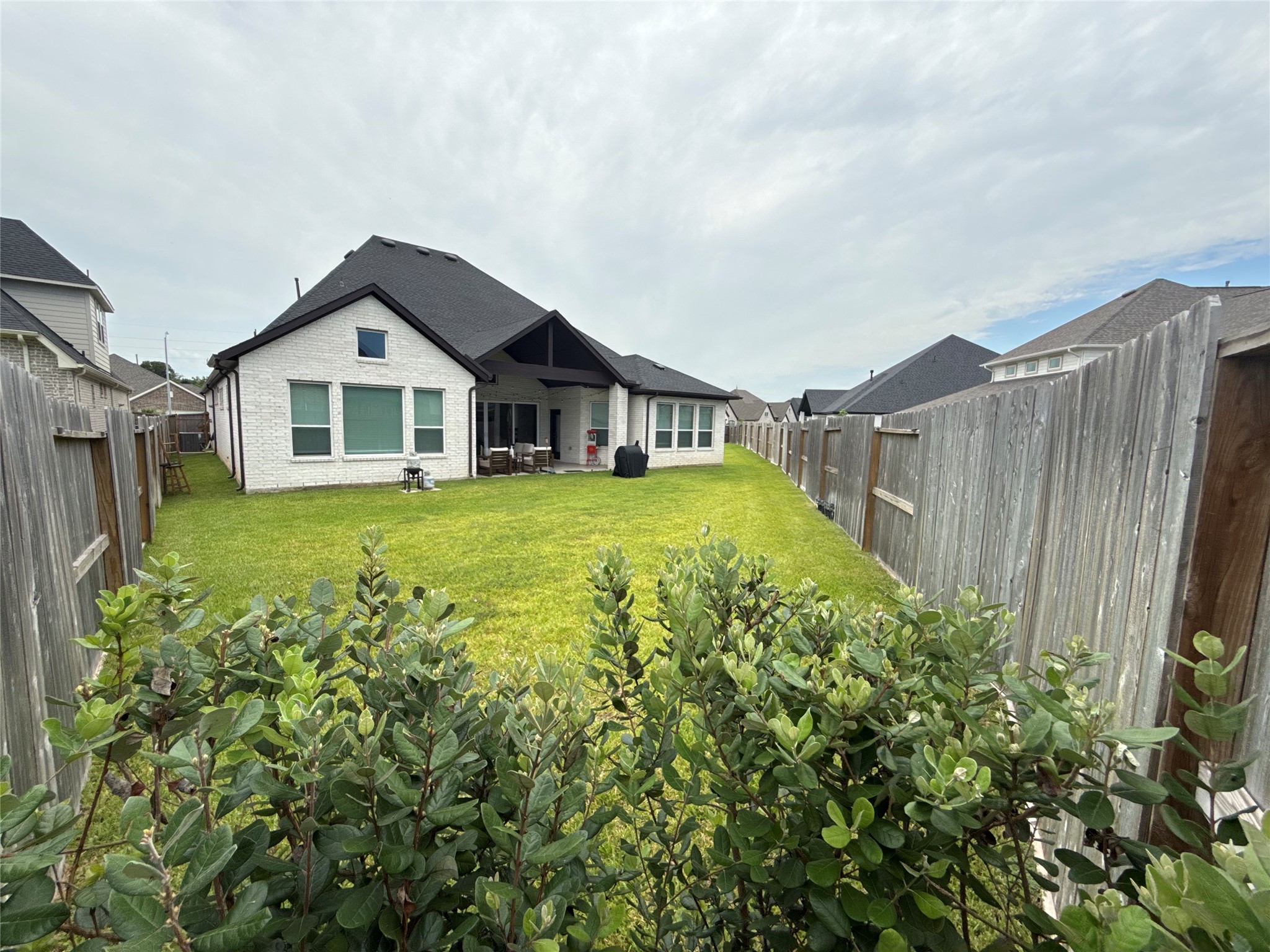 Spacious fenced backyard with lush greenery, perfect for outdoor gatherings and relaxation, complemented by a charming brick exterior and covered patio area.