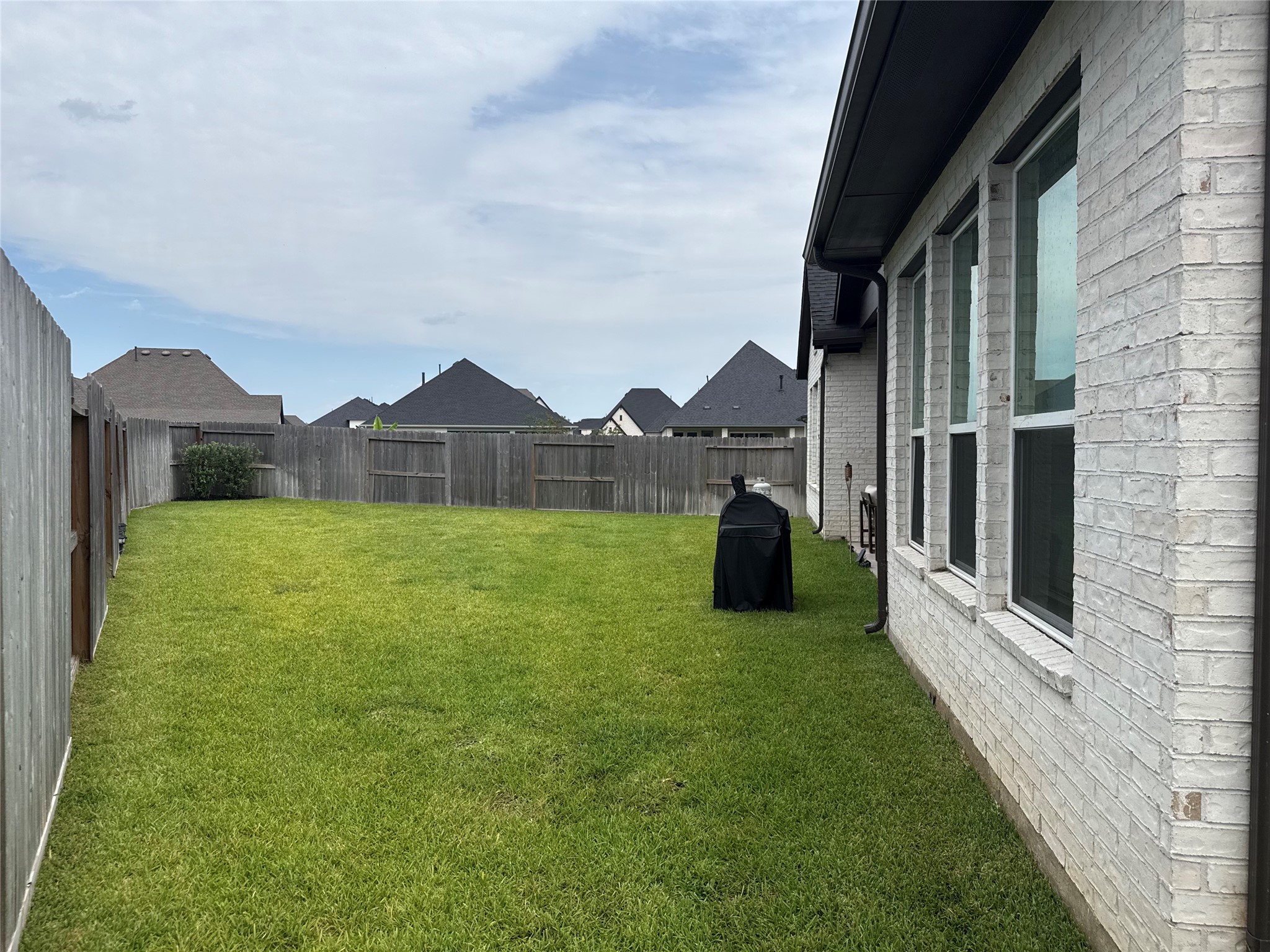 Spacious backyard with well-maintained lawn, privacy fencing, and a side view of the home's brick exterior featuring large windows, perfect for outdoor activities and relaxation. Spacious backyard with well-maintained lawn, privacy fencing, and a side view of the home's brick exterior featuring large windows, perfect for outdoor activities and relaxation.