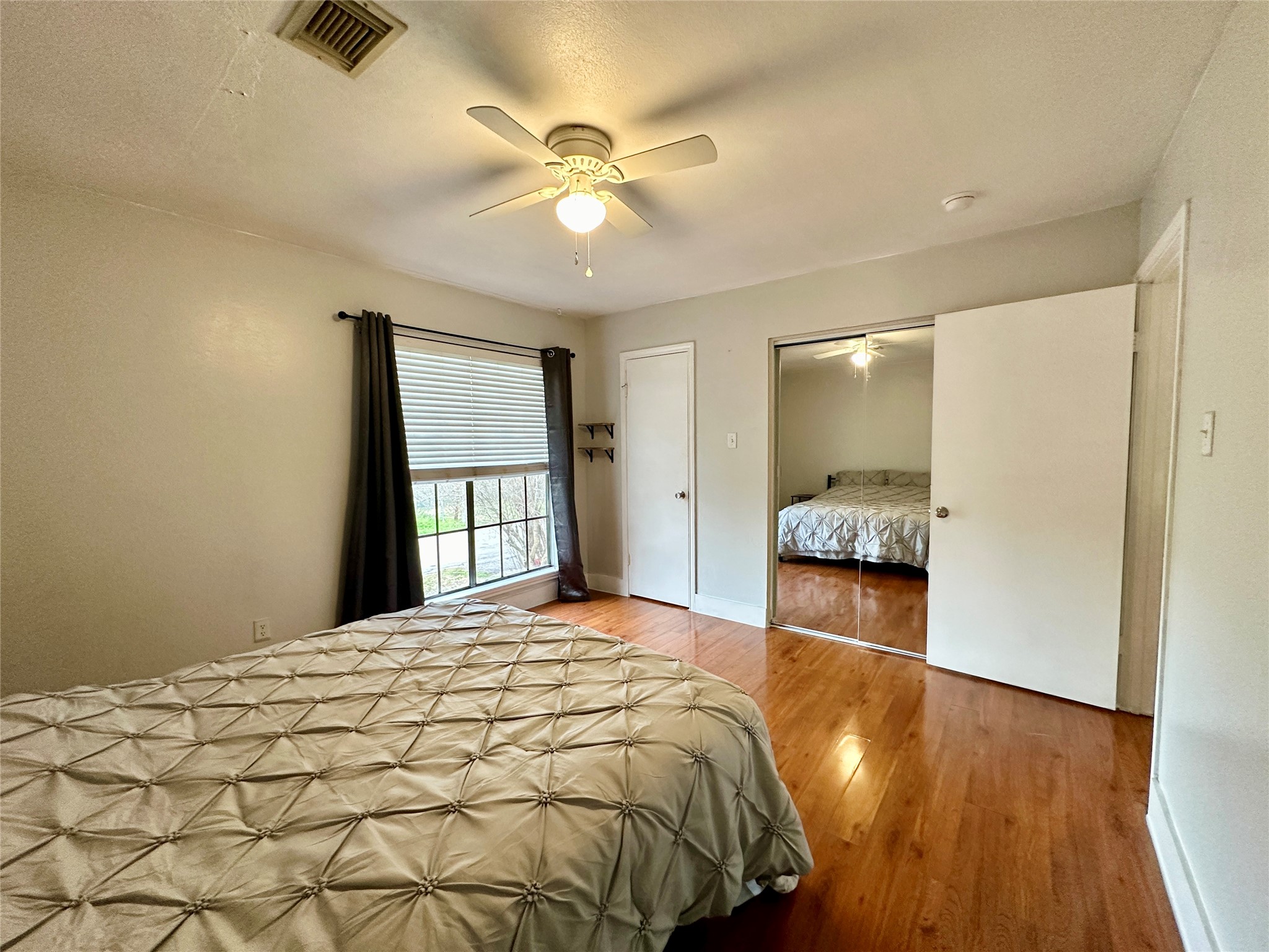 Primary bedroom features closet w/ full length mirrored sliding doors, hard flooring, lighted ceiling fan.