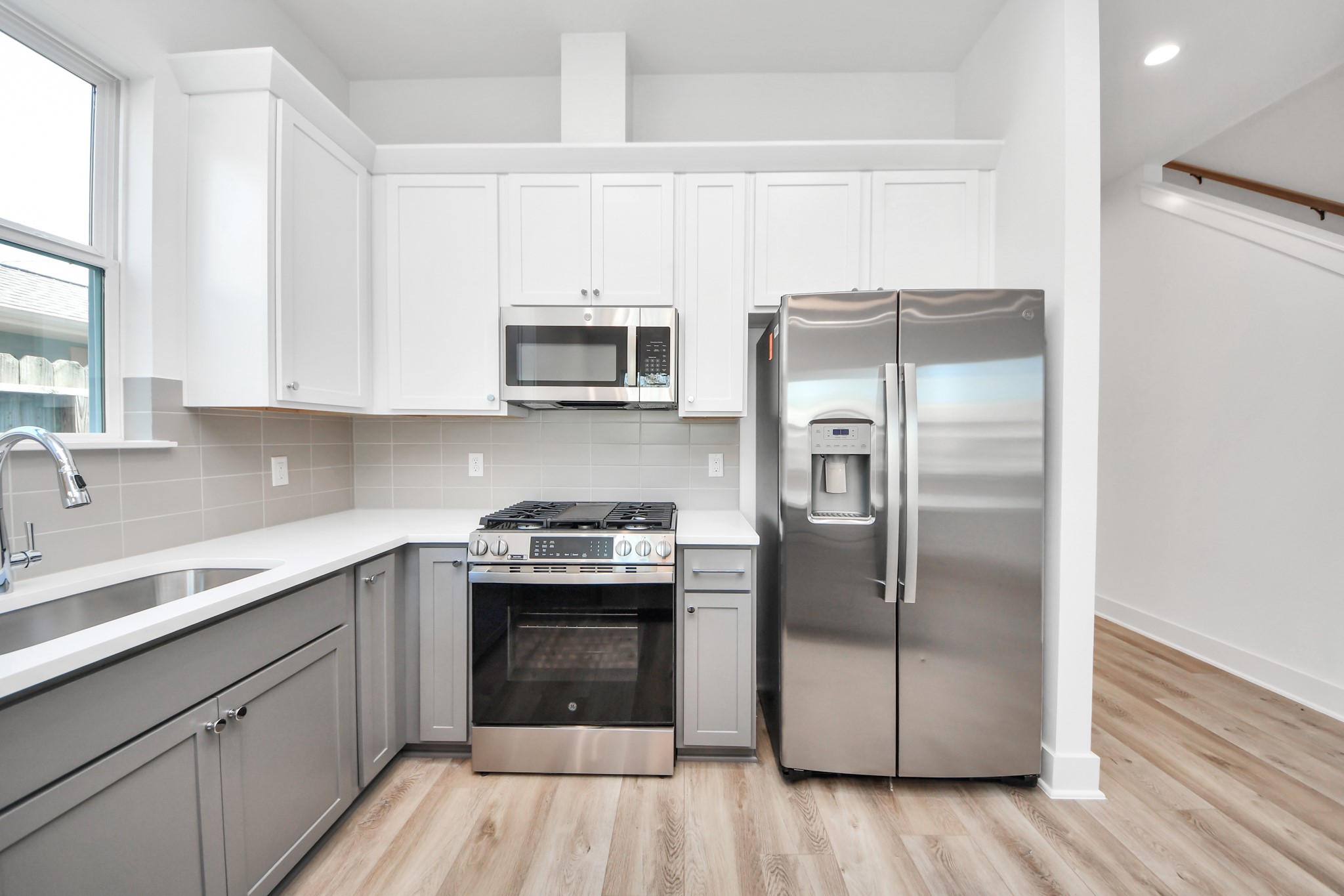 Unit B kitchen featuring white cabinetry, gray lower cabinets, and stainless steel appliances.