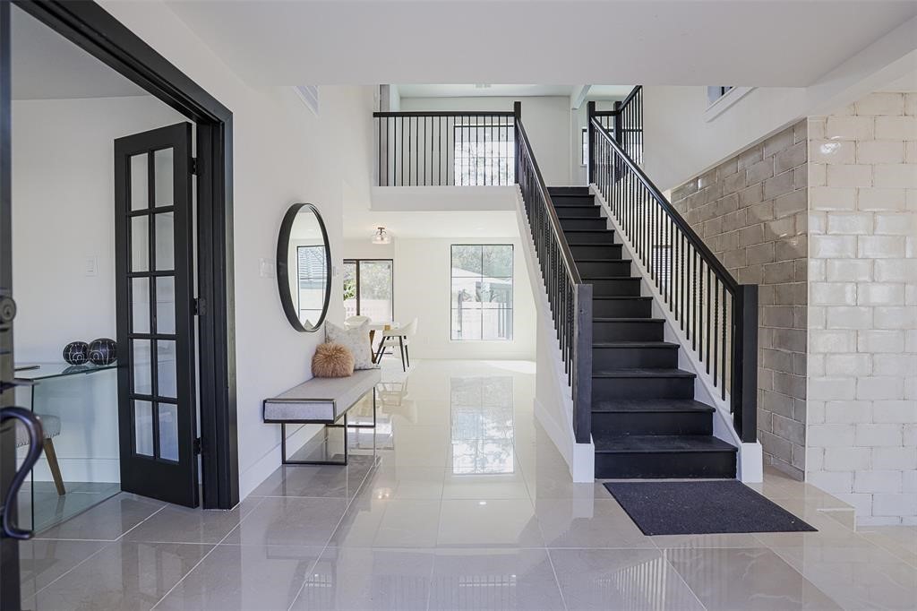 Grand entryway featuring striking tile flooring and a dramatic black wooden staircase that anchors the space with timeless elegance. Soaring ceilings and abundant natural light enhance the luxurious feel of this sophisticated welcome into the home. Grand entryway featuring striking tile flooring and a dramatic black wooden staircase that anchors the space with timeless elegance. Soaring ceilings and abundant natural light enhance the luxurious feel of this sophisticated welcome into the home.