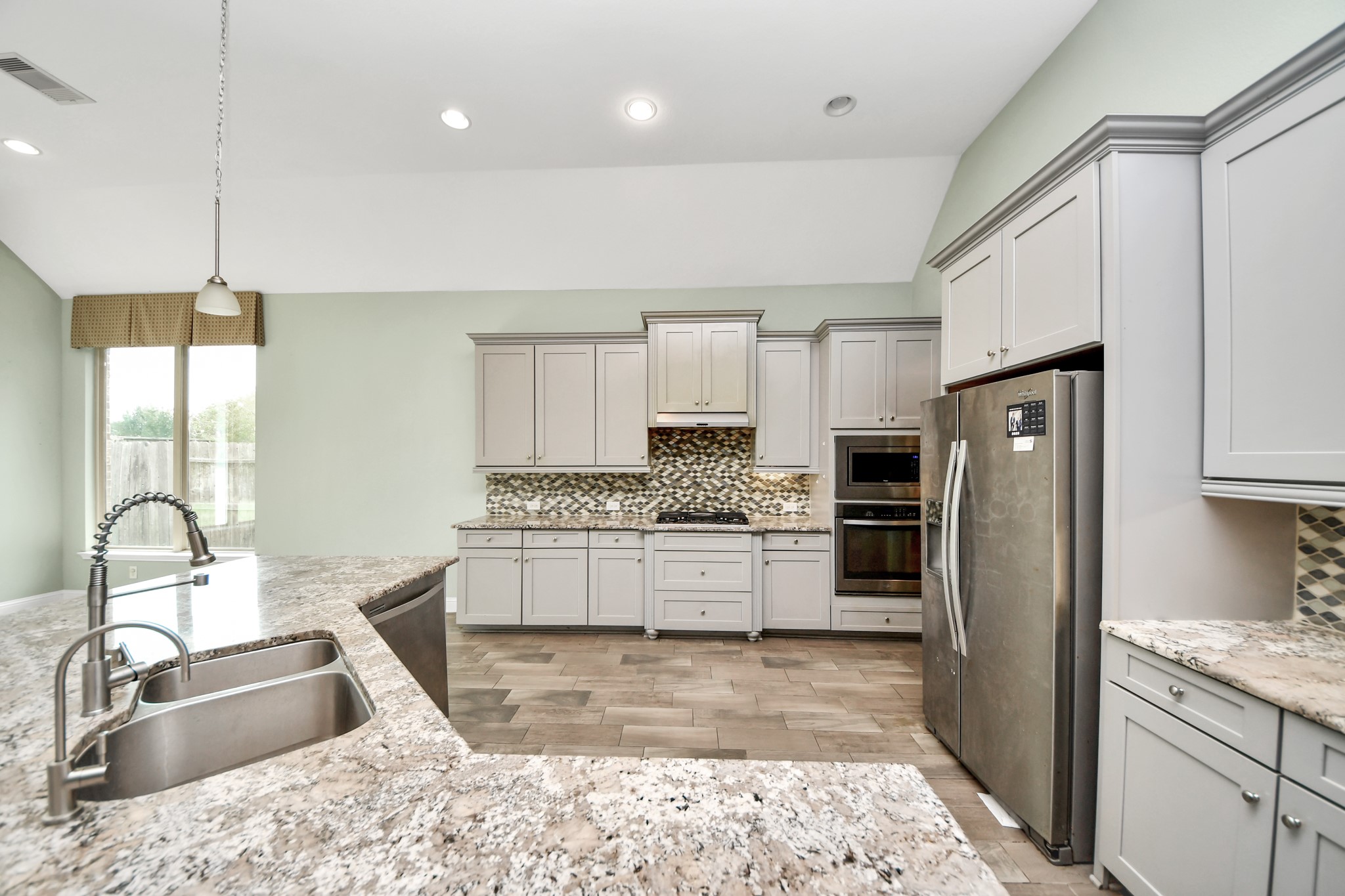 Well-appointed kitchen with extensive cabinetry, granite countertops, mosaic tile backsplash, stainless steel appliances, and generous workspace.