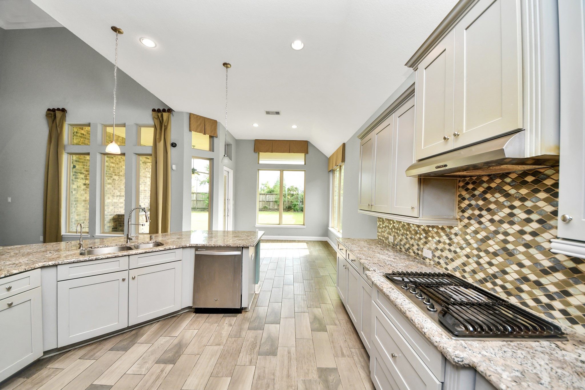 Granite countertops, gas cooktop, decorative mosaic backsplash, plentiful cabinetry, and bright natural light highlight this functional kitchen.